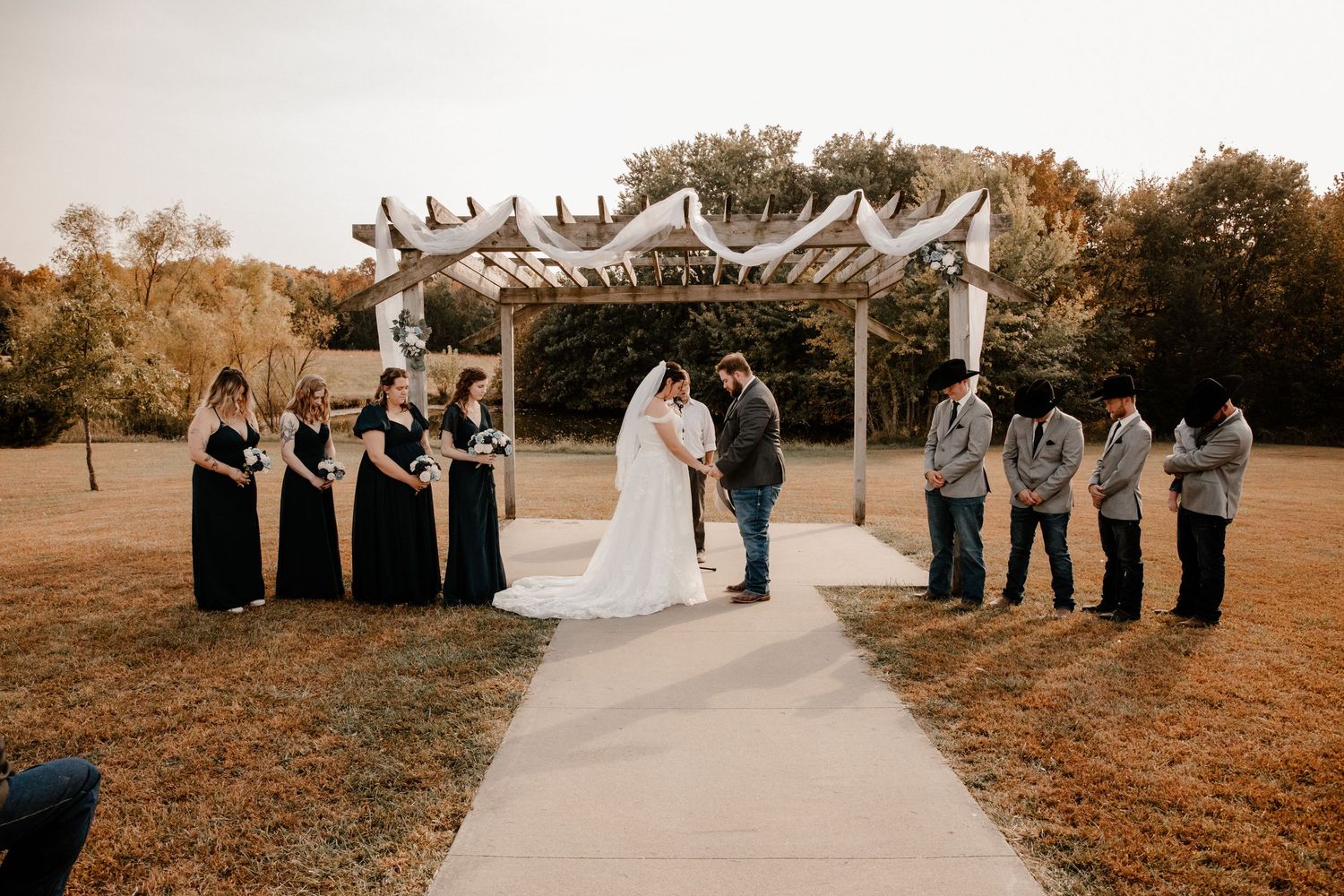 Wedding ceremony setup with white chairs and floral arch in an outdoor garden setting.