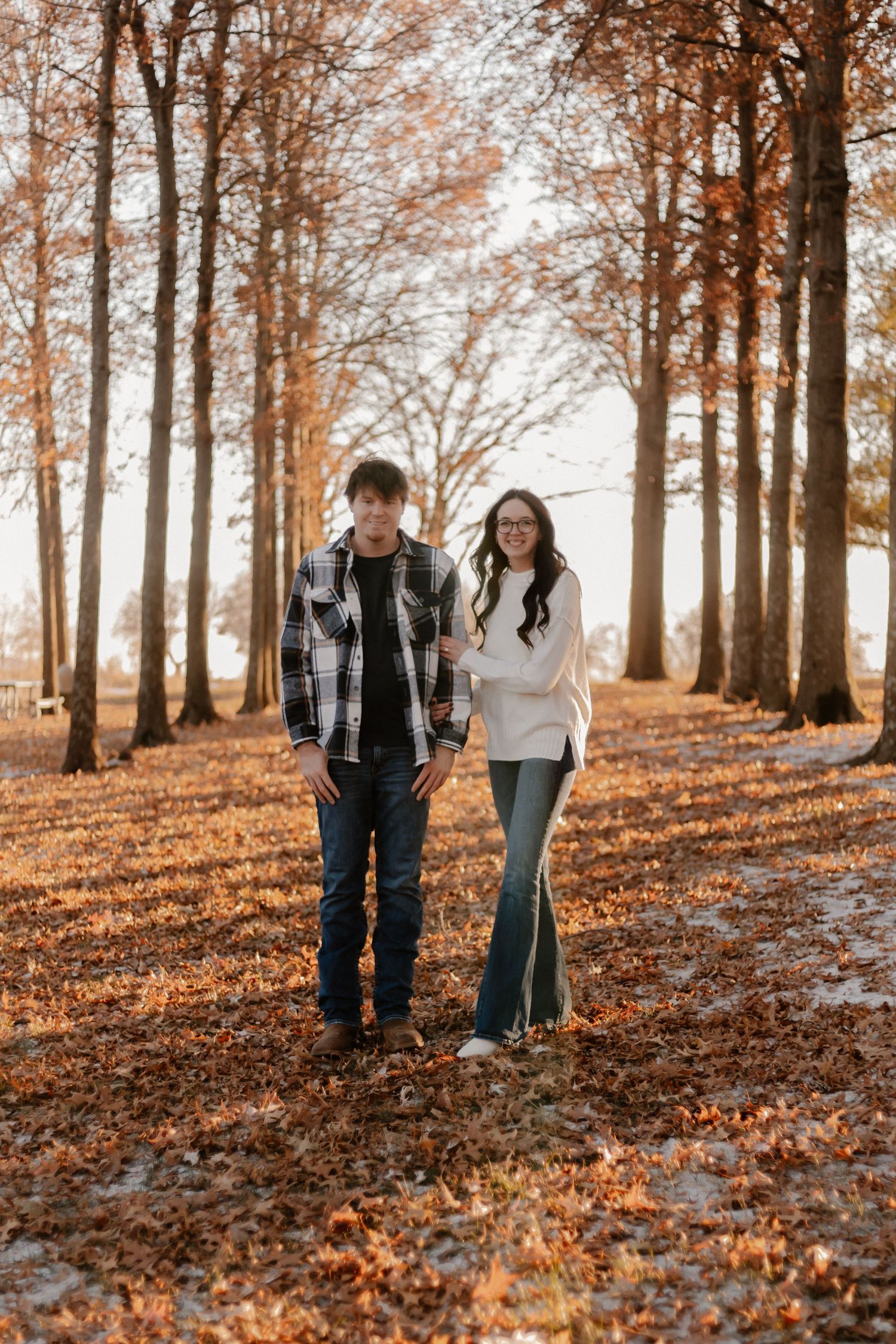 Couple walking through a forest path covered in fallen autumn leaves.