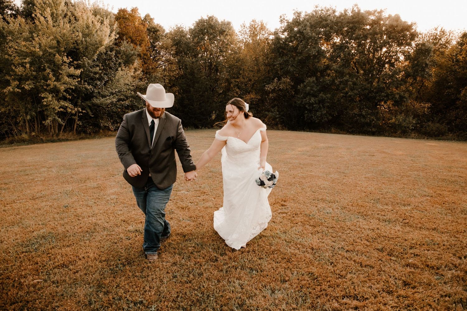 A couple dances and spins in a golden autumn field at sunset during their wedding celebration.
