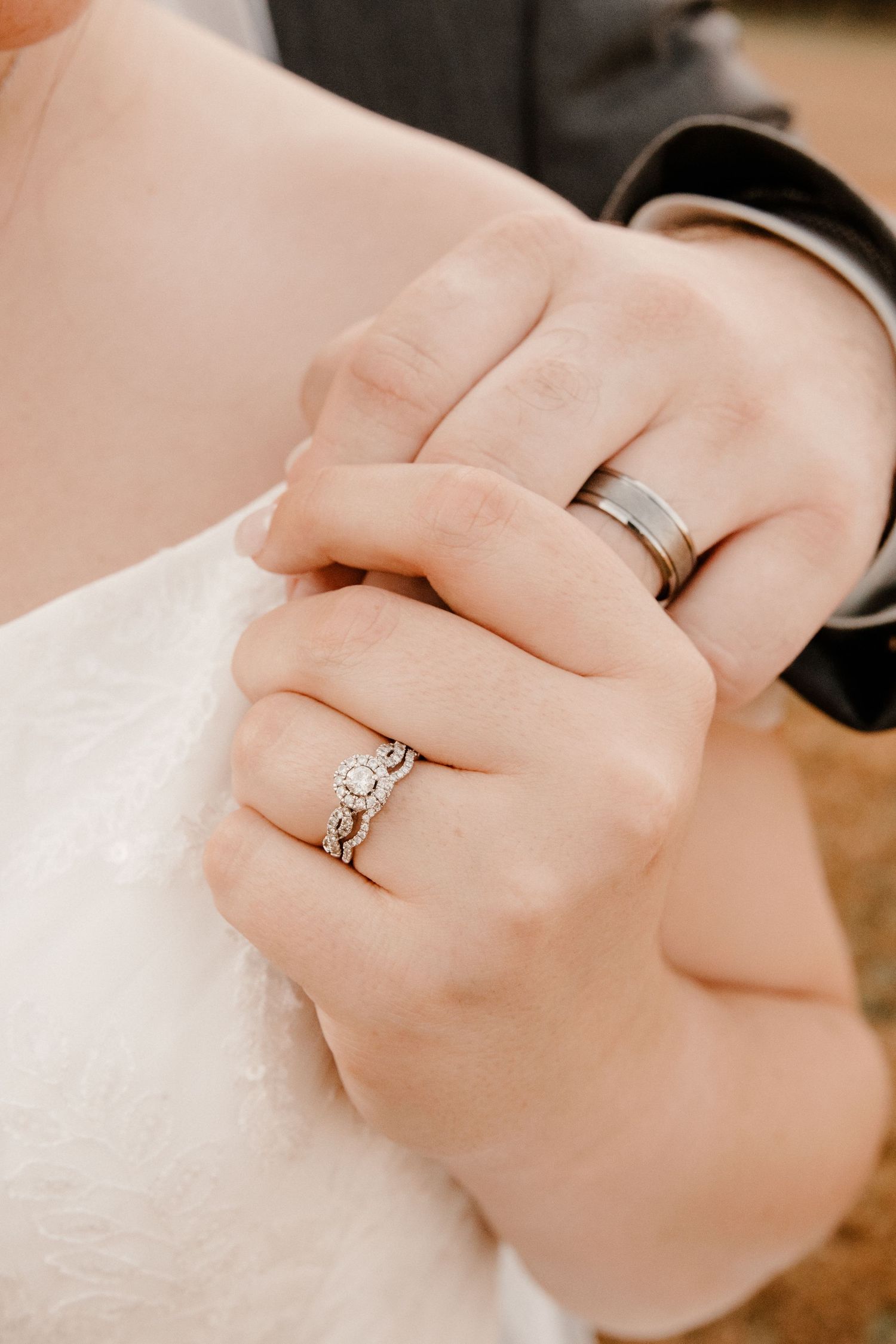 Close-up of wedding rings with bride wearing white dress and groom in black suit.