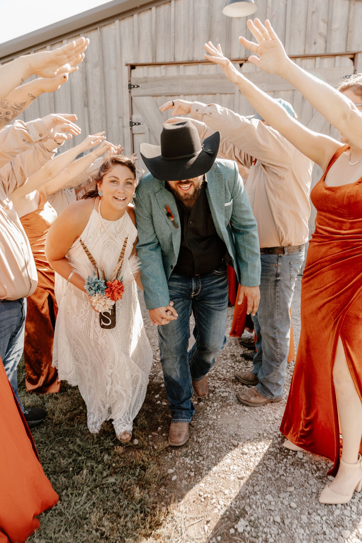Wedding party strikes fun poses against rustic barn wall wearing mix of formal attire.