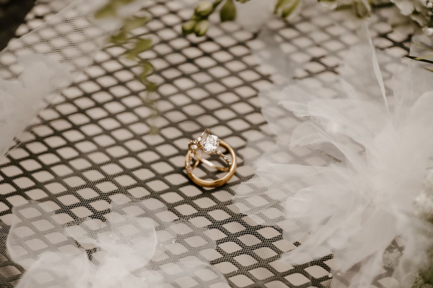 Wedding rings and delicate veil detail shot on textured metallic surface.