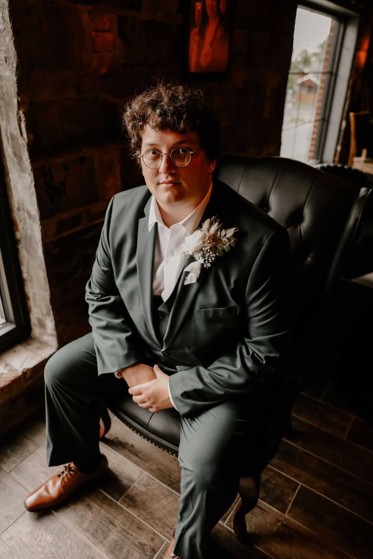 Wedding attire detail shot showing formal suit and boutonniere in moody indoor lighting.