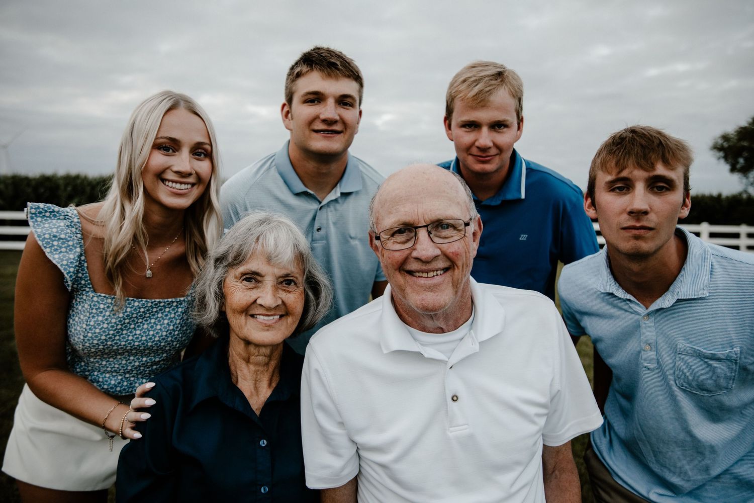 Multi-generational family group poses together outdoors wearing coordinating blue and white outfits.