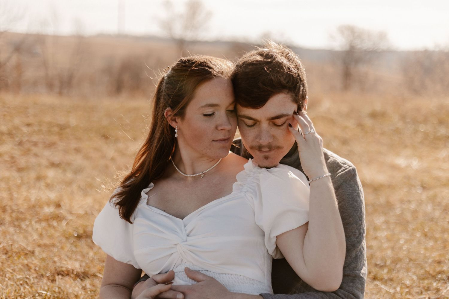 A couple shares a tender embrace in a golden field, the bride in white and groom in gray suit.