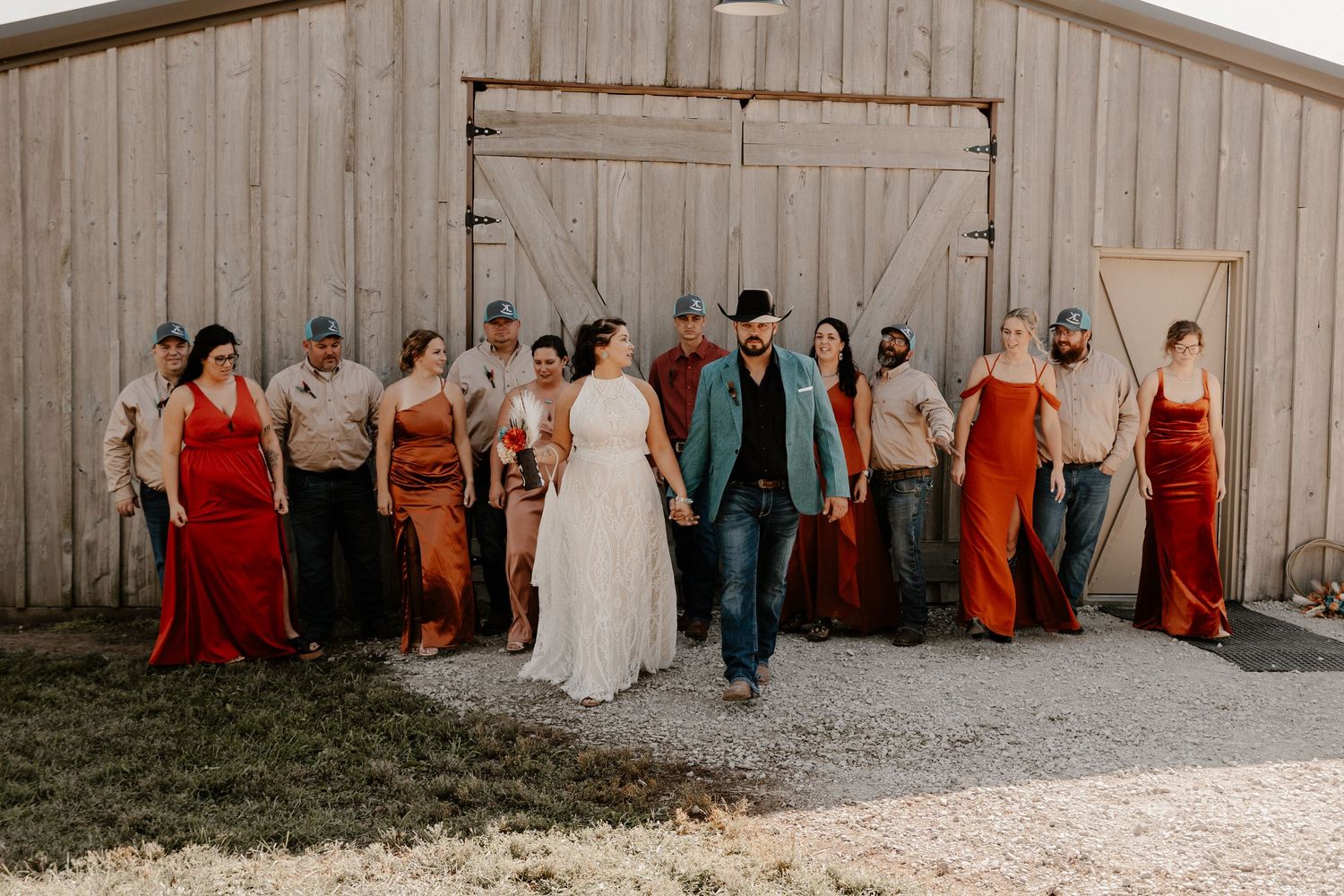 Wedding party poses in front of rustic barn wearing coordinated red and neutral attire.