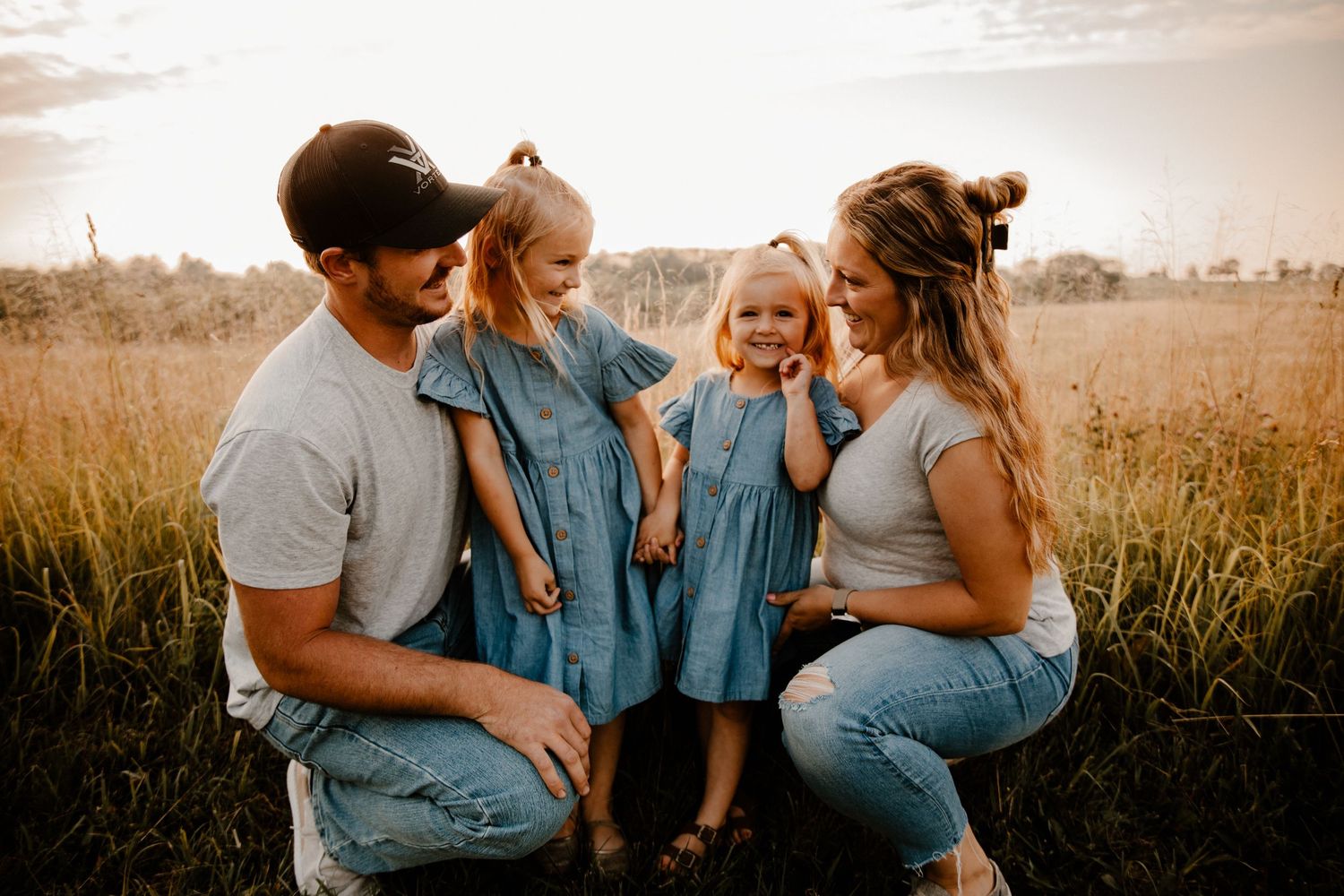 Family members in denim and casual wear sit together in a golden field at sunset.