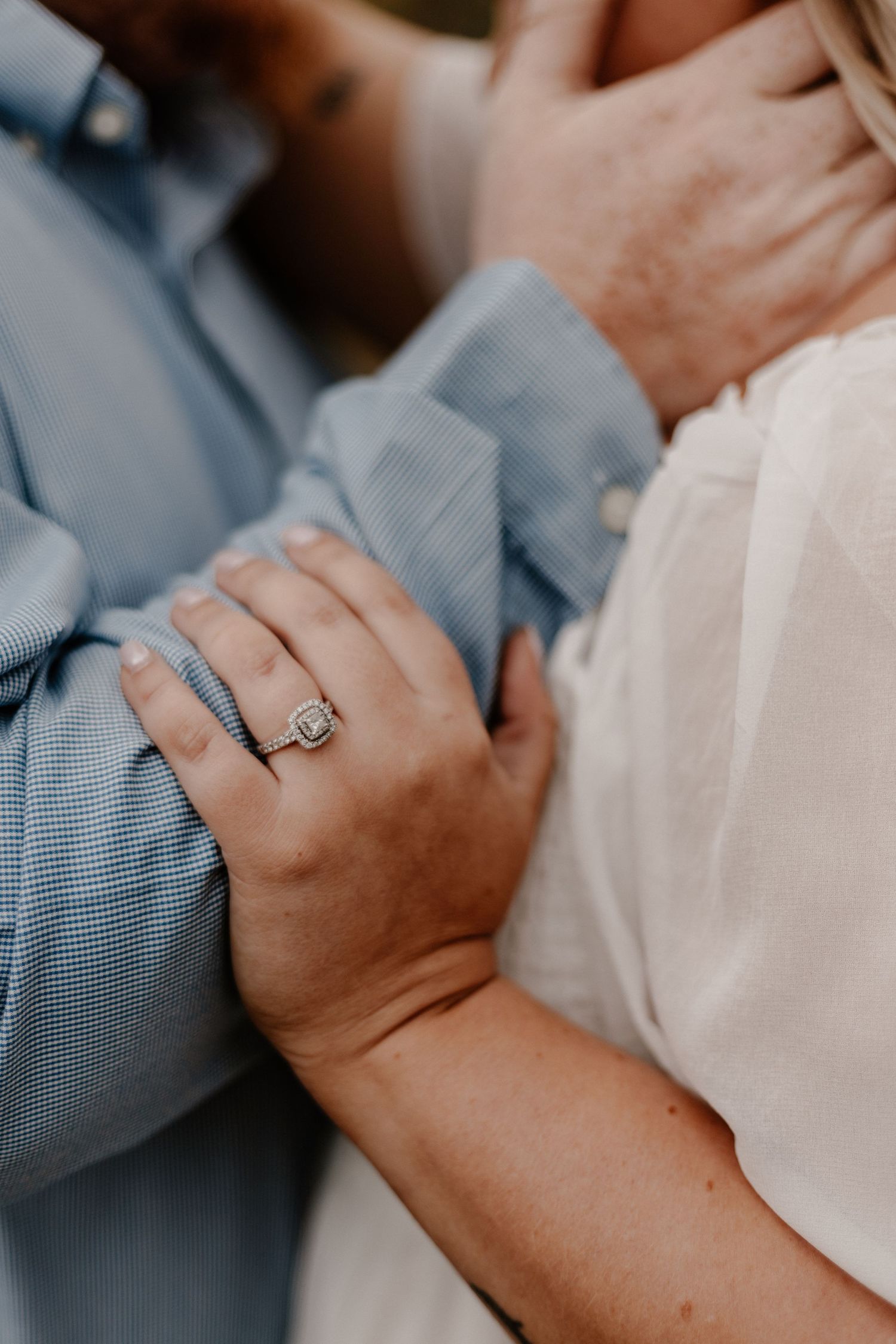 Couple's hands intertwined showing engagement ring detail in soft lighting.