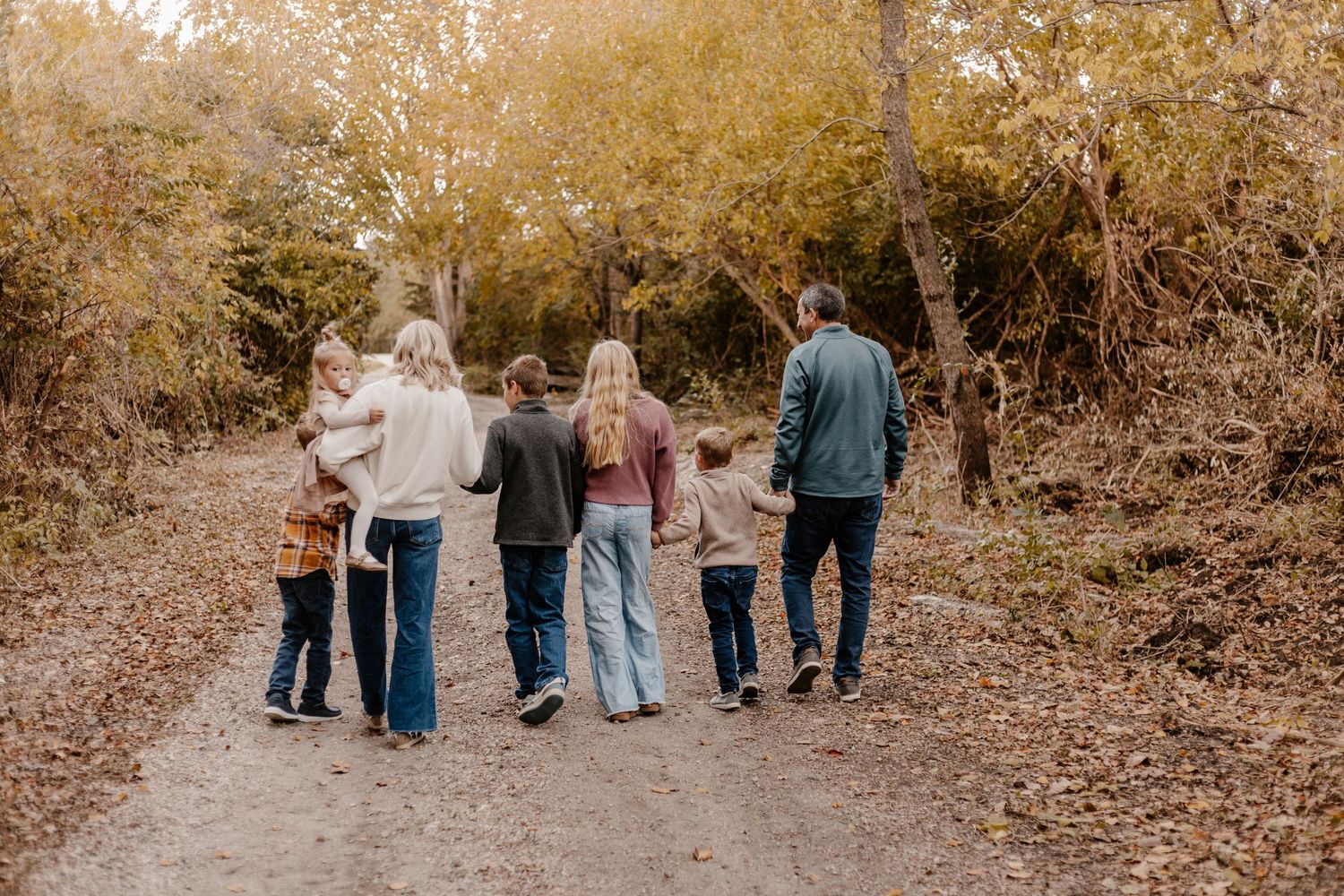 Family walking together hand in hand on tree-lined path during fall season.