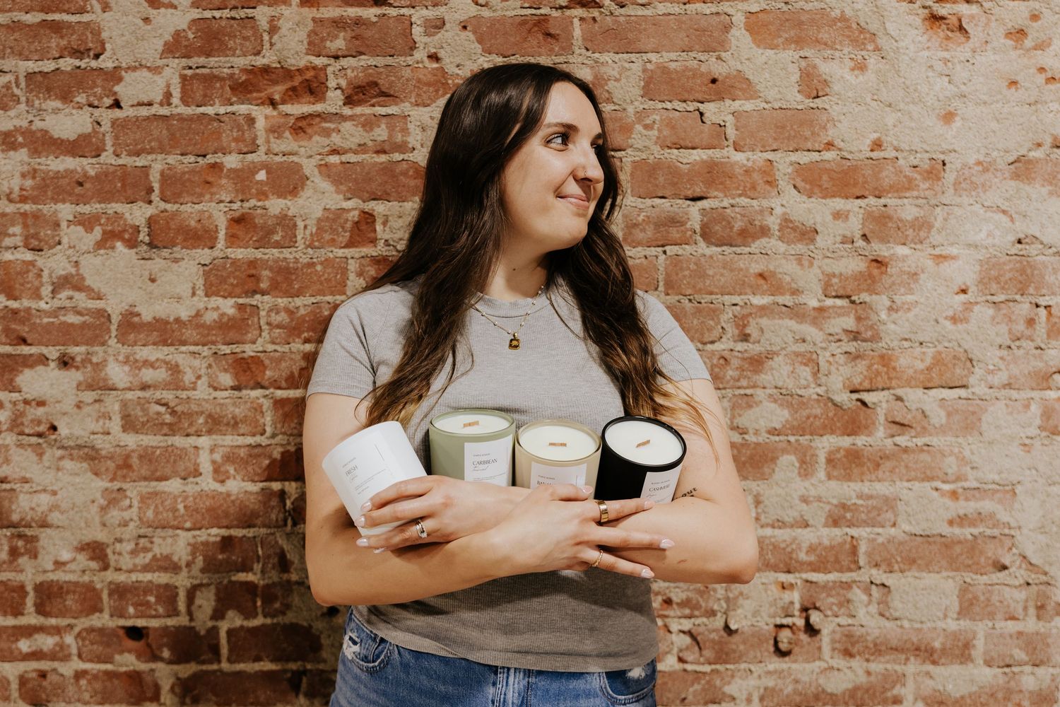 Woman in gray tee holding candles against brick wall.