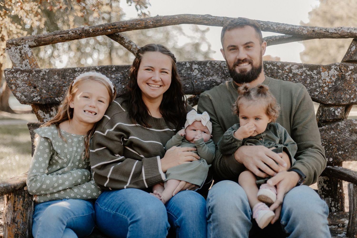 Family of five sitting together on rustic wooden bench during outdoor portrait session.