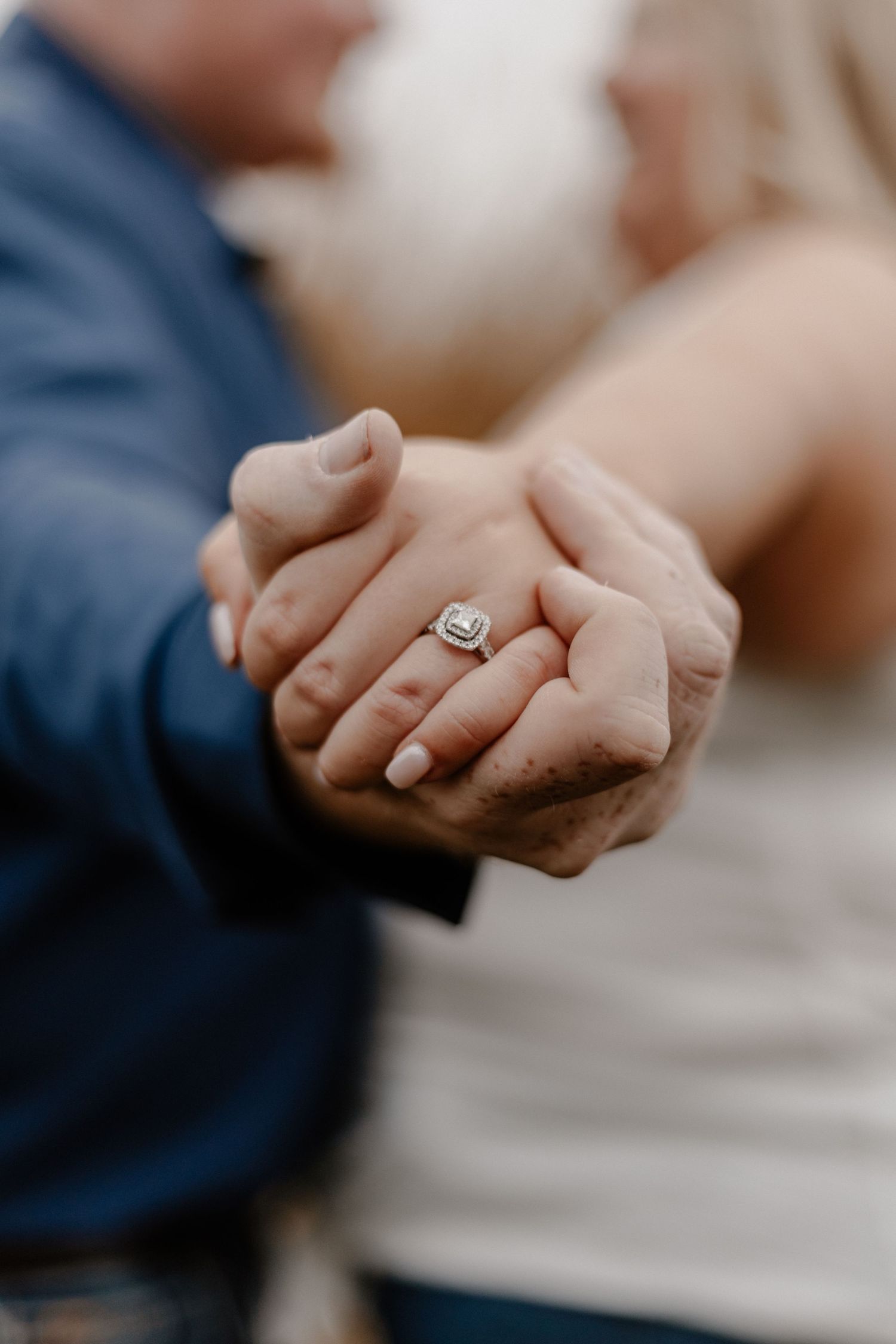 Close-up of hands holding each other with diamond engagement ring.