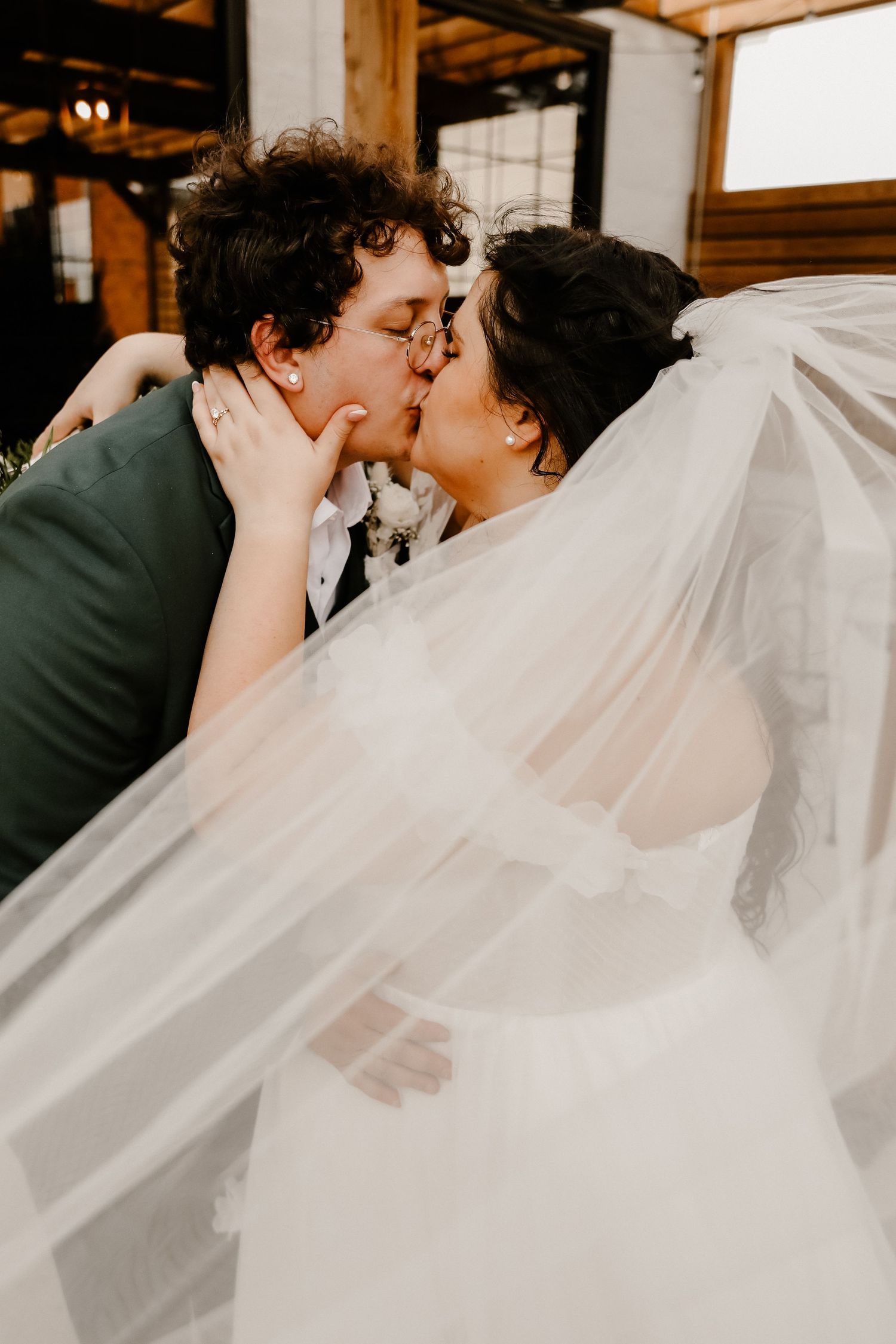 Romantic moment captured through flowing white veil in rustic wooden venue setting.