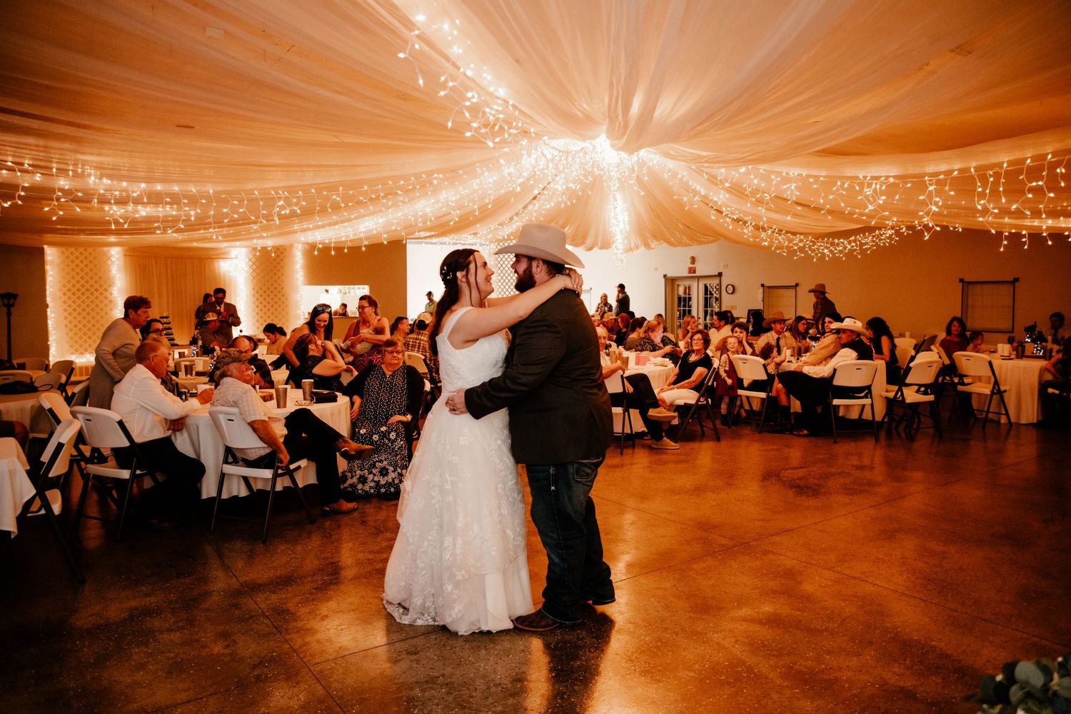 Wedding couple shares first dance under twinkling lights in elegant reception venue.