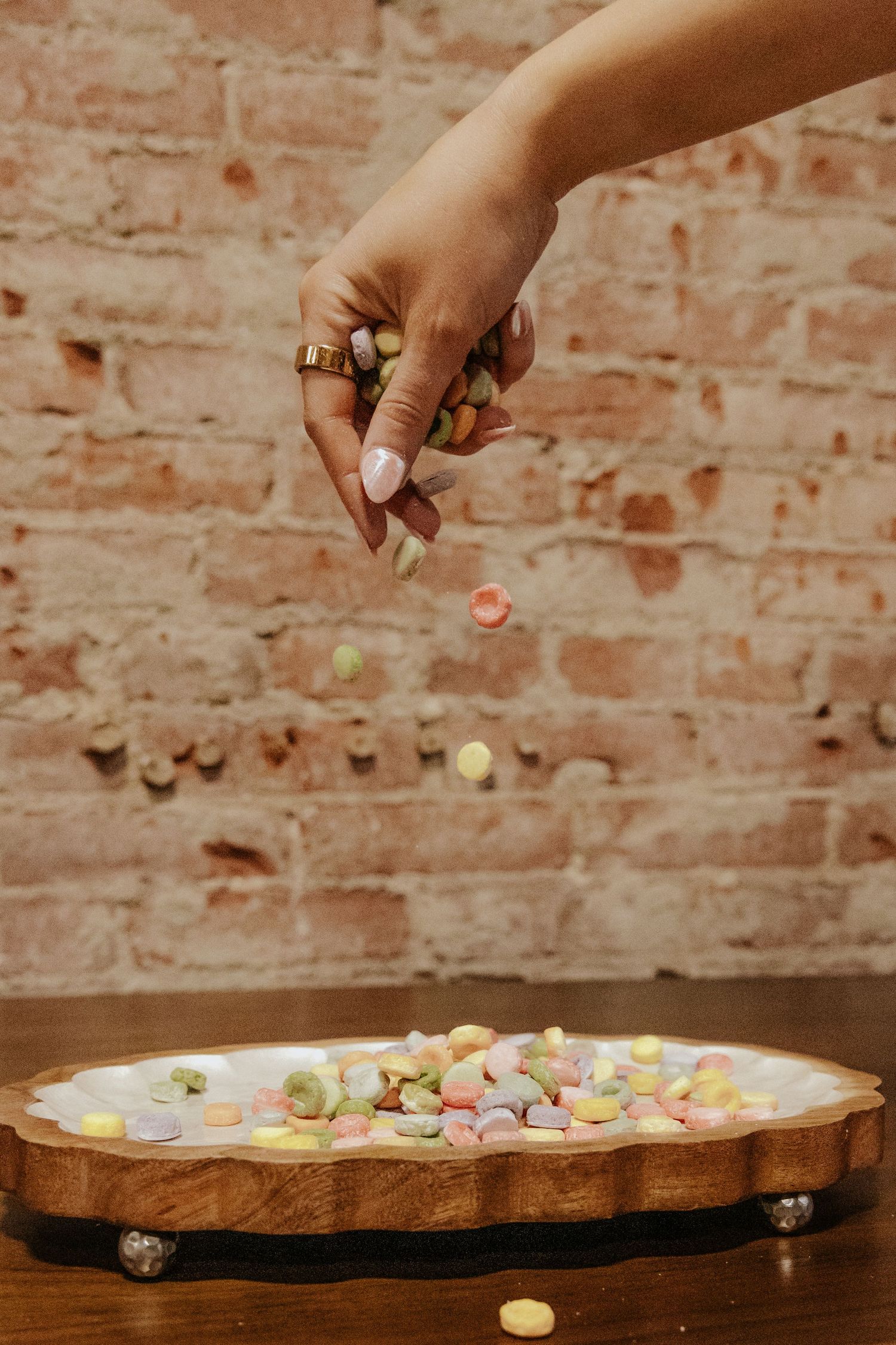 Hand dropping colorful candy onto decorative wooden tray.