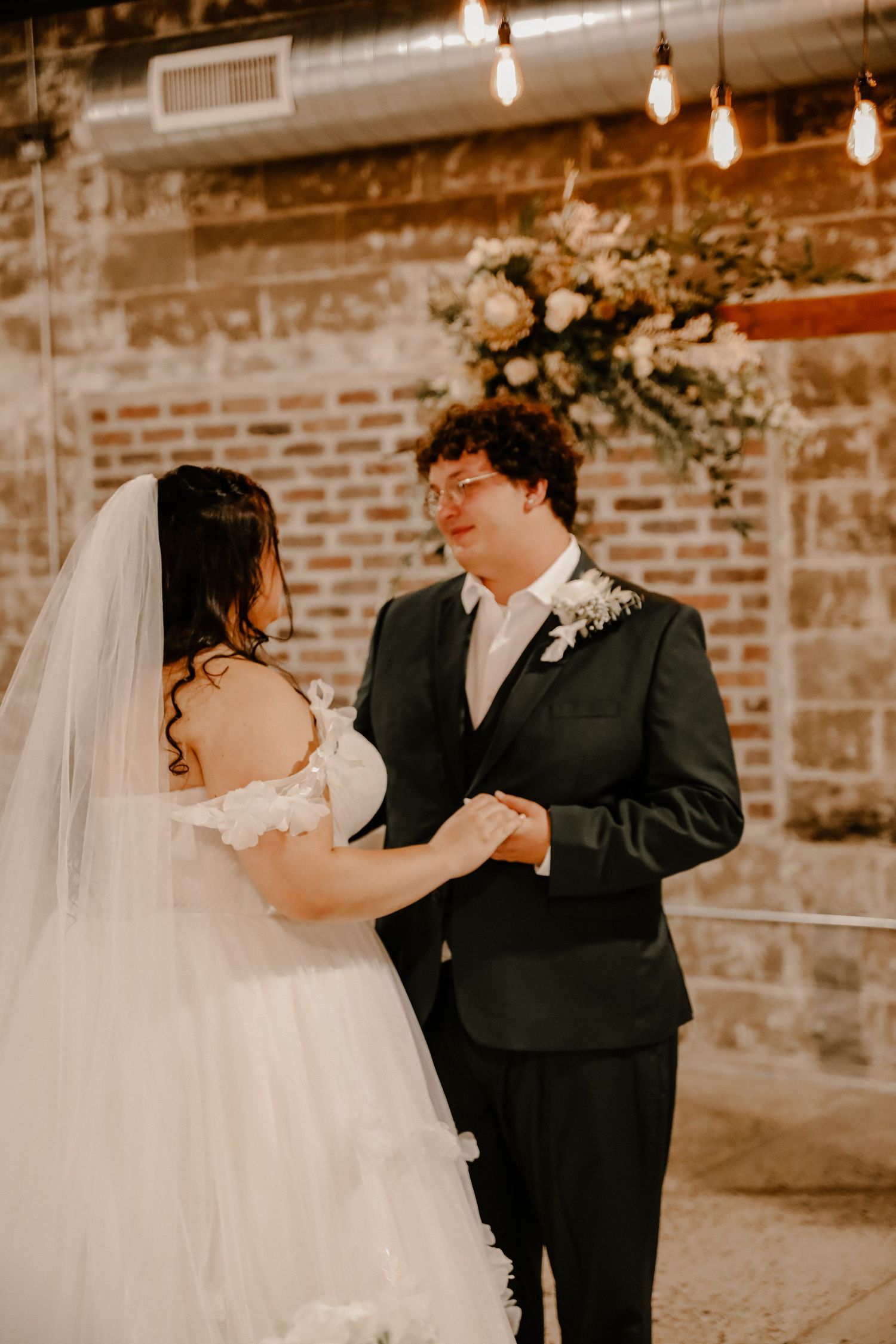 Couple sharing an intimate dance moment in a rustic brick-walled venue with string lights.
