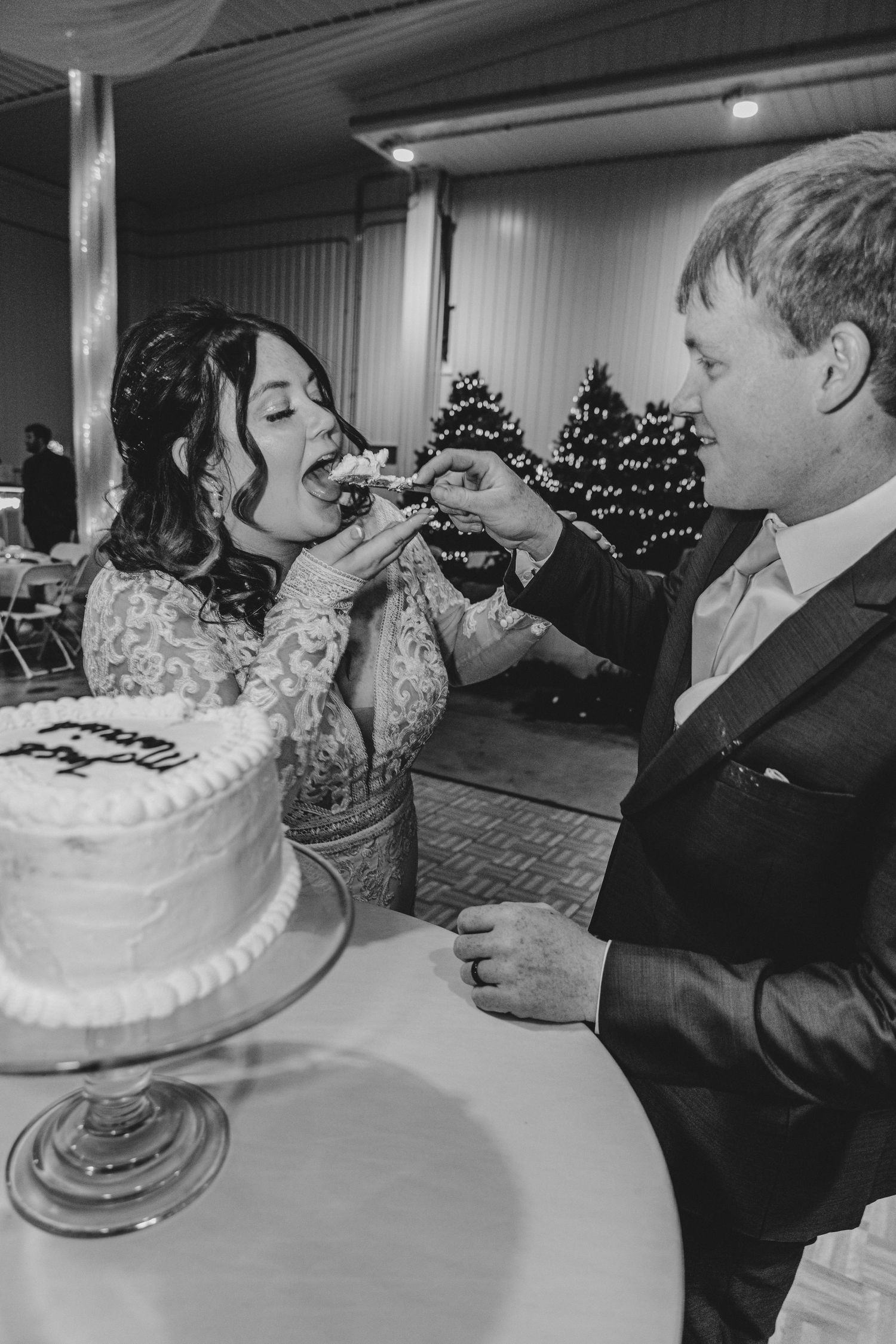 Wedding couple playfully feeds each other cake during traditional cake cutting ceremony.