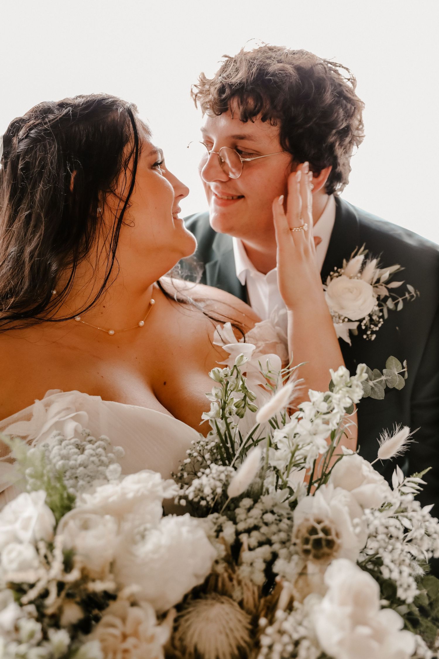 An intimate wedding portrait showing tender interaction between newlyweds with white floral bouquet details.