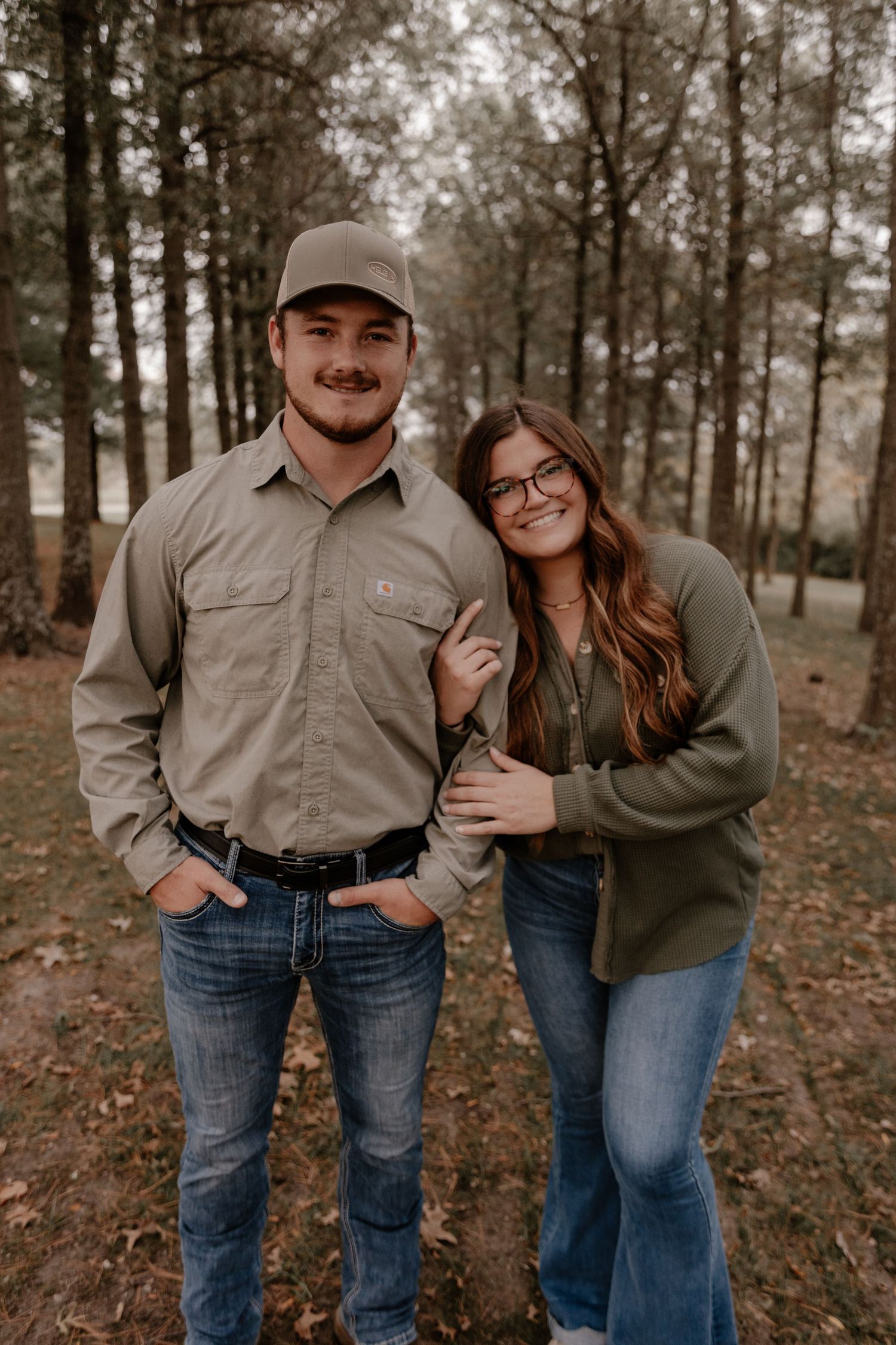Couple embracing in wooded area wearing casual attire.