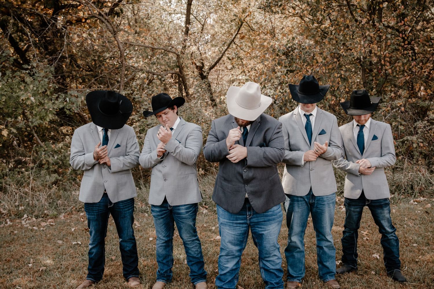 Groomsmen in matching gray suits and cowboy hats pose looking down at ground.