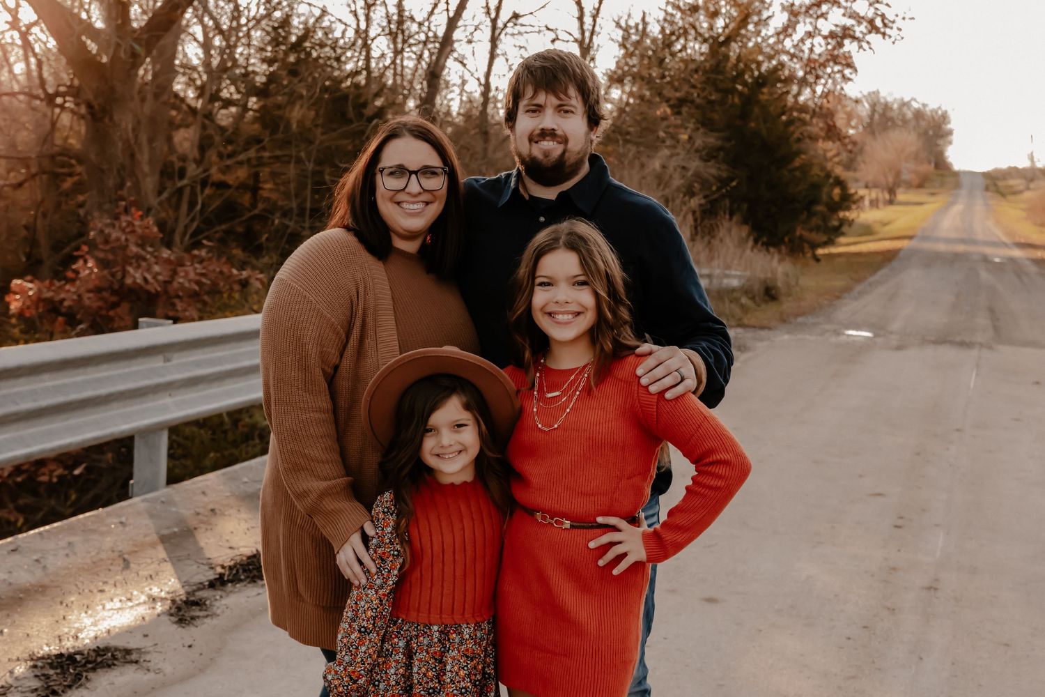 Autumn family portrait of four people wearing coordinating red and brown outfits on a country road.