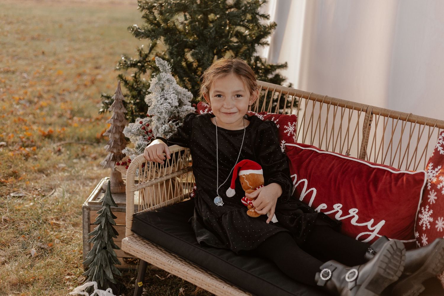 Young child in black clothing sitting on wooden bench with holiday decor and holding a mug.