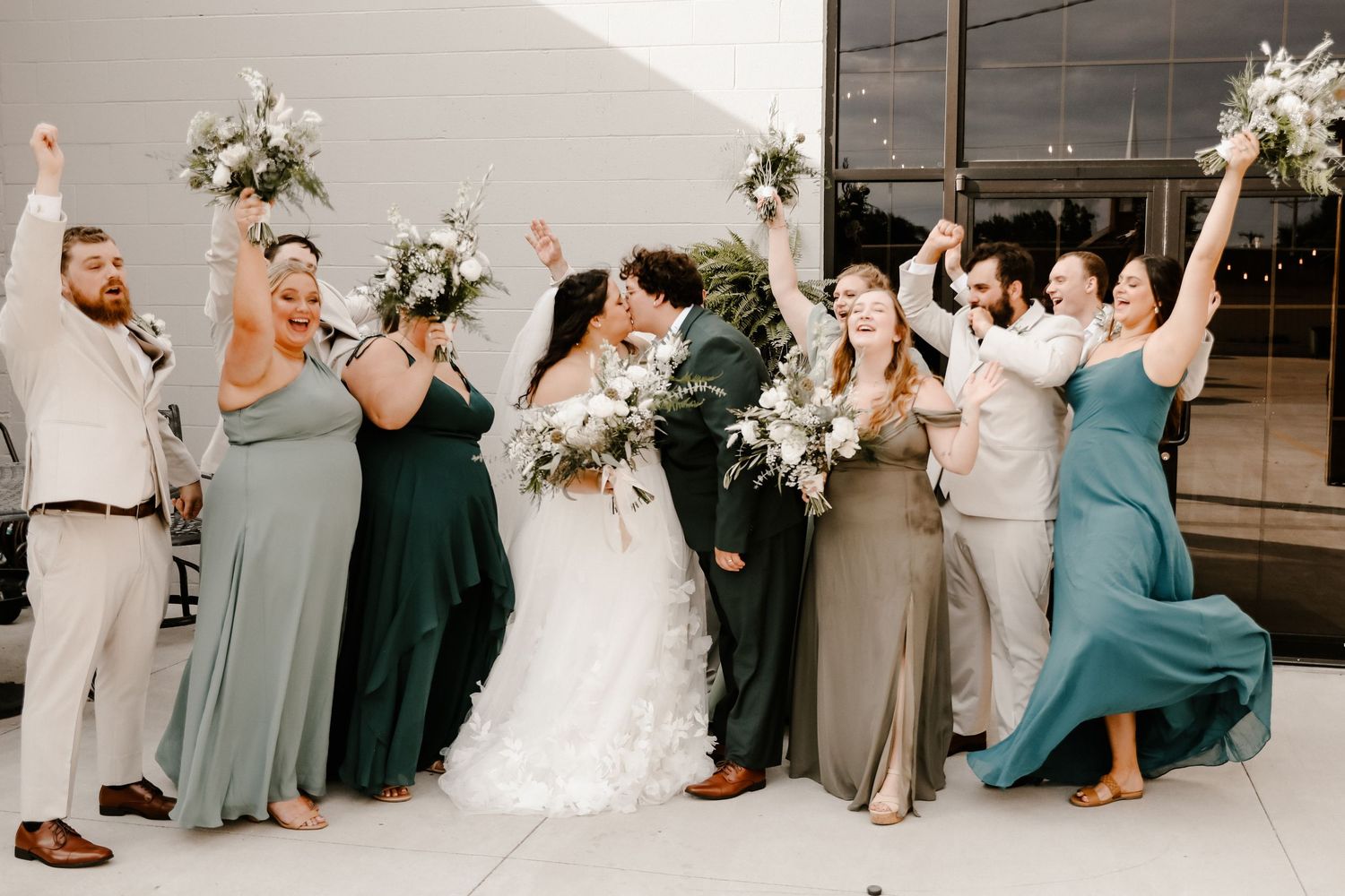 Wedding party in coordinated teal and grey dresses posing together in celebration.