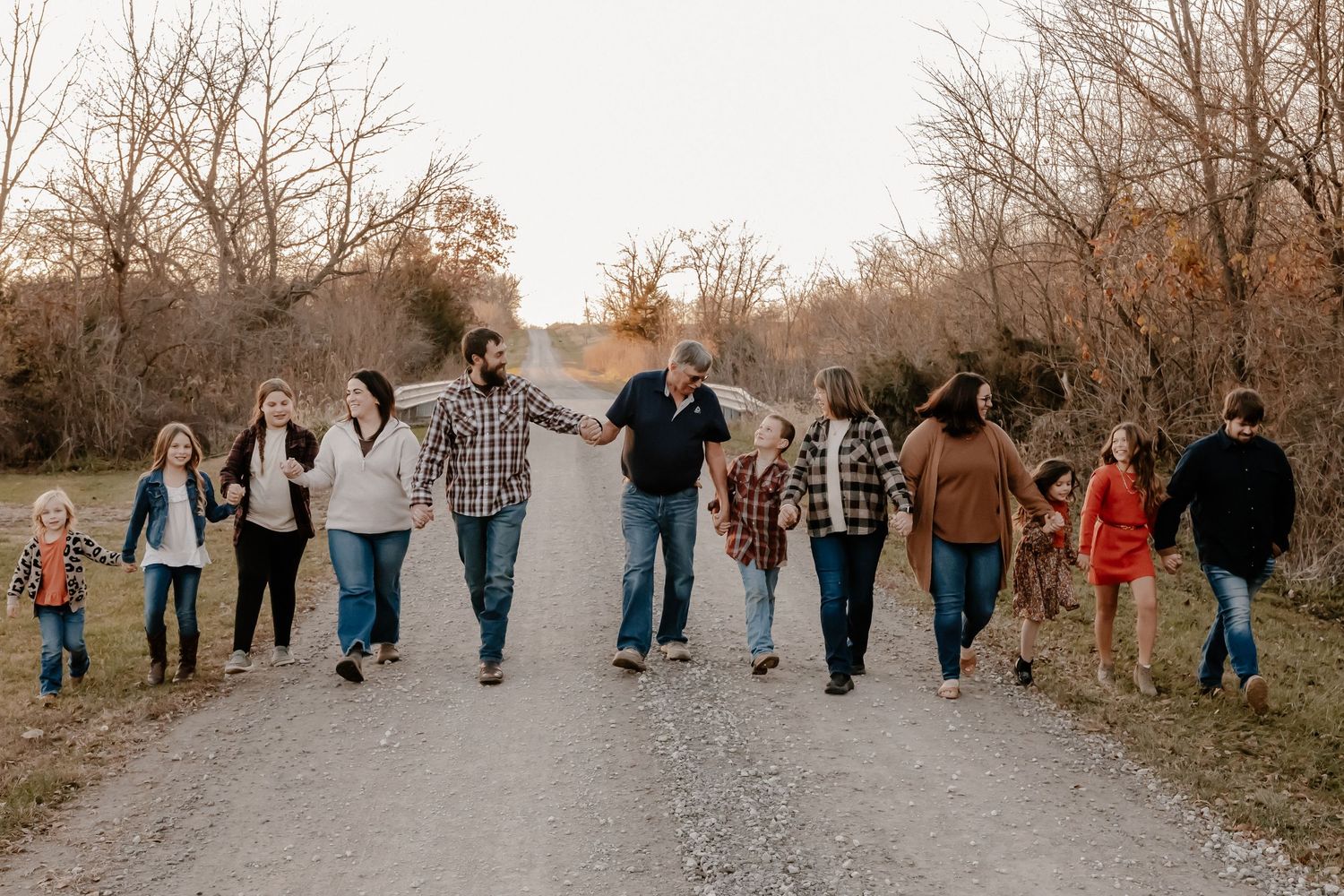 Large group walking together on a gravel road during fall with bare trees in background.