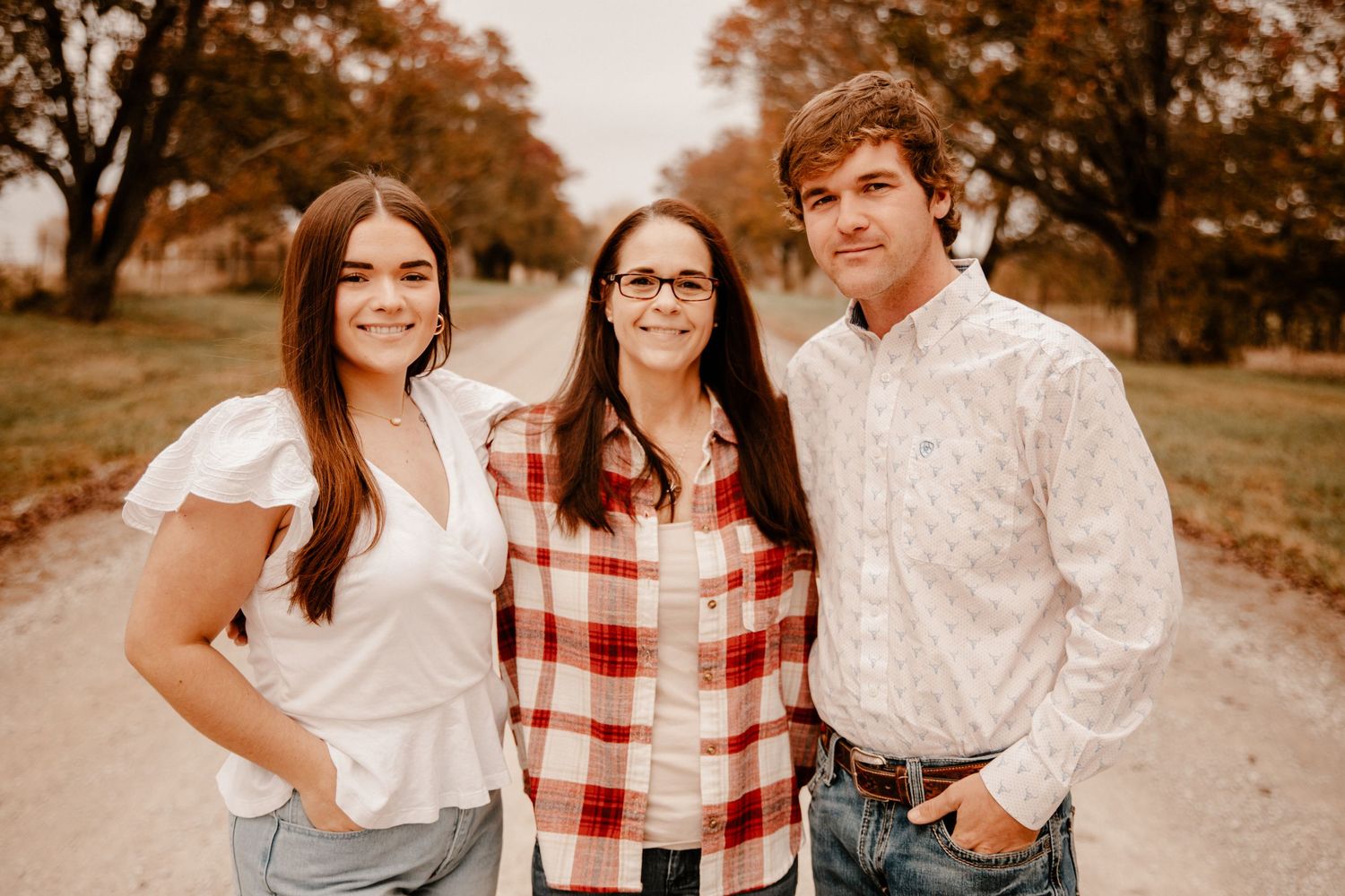 Three people wearing casual plaid and white clothing pose together outdoors in autumn.