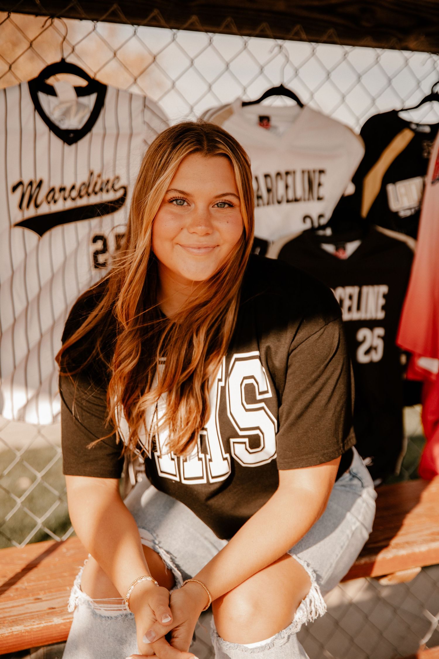 Athletic-themed photo shoot with baseball jerseys and chain link fence backdrop.