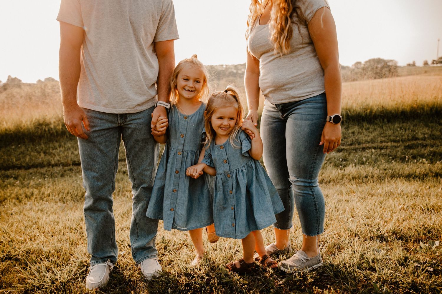 Family wearing coordinated denim outfits in sunset field.