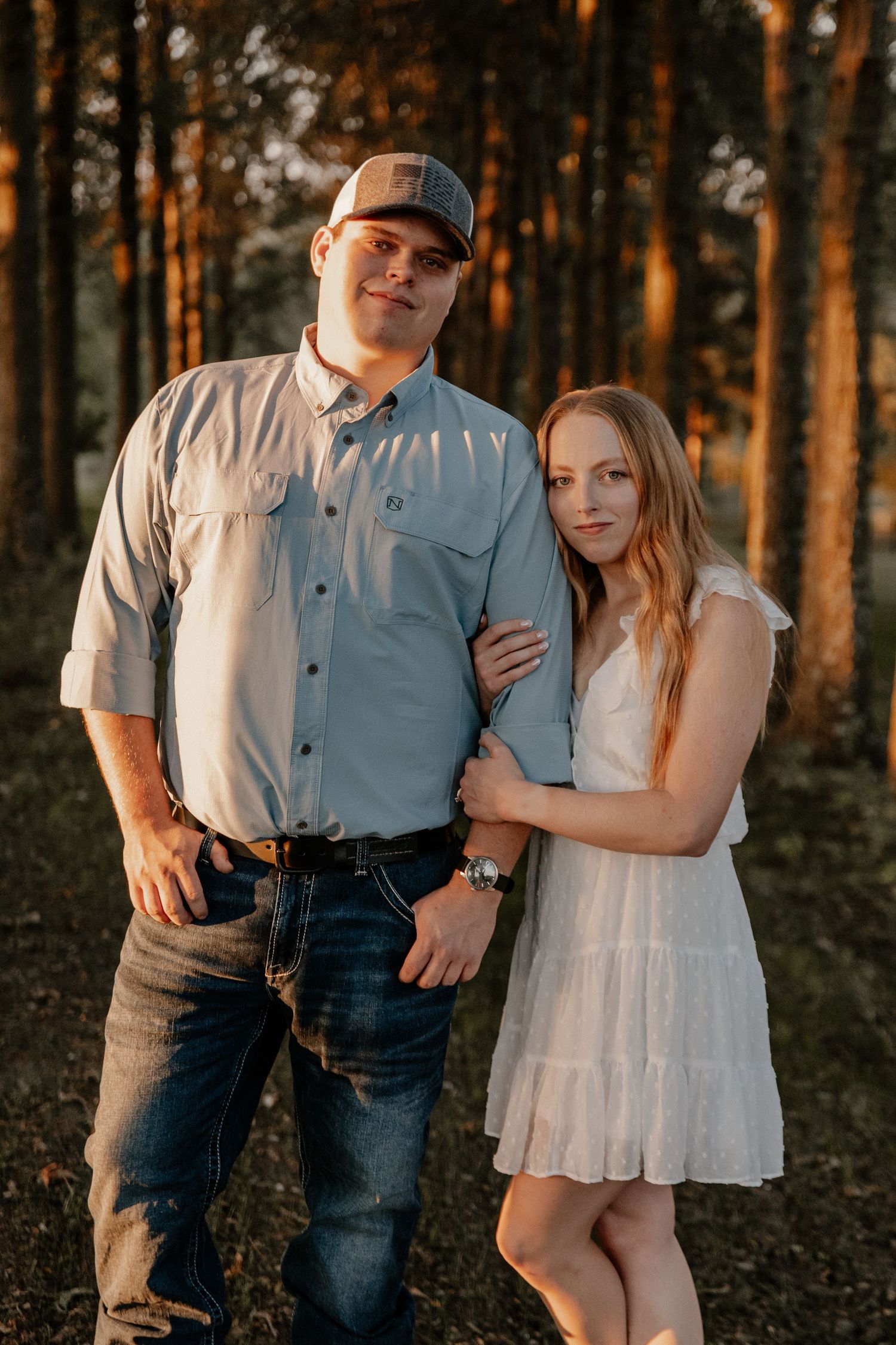 A couple poses together in a wooded area during golden hour.