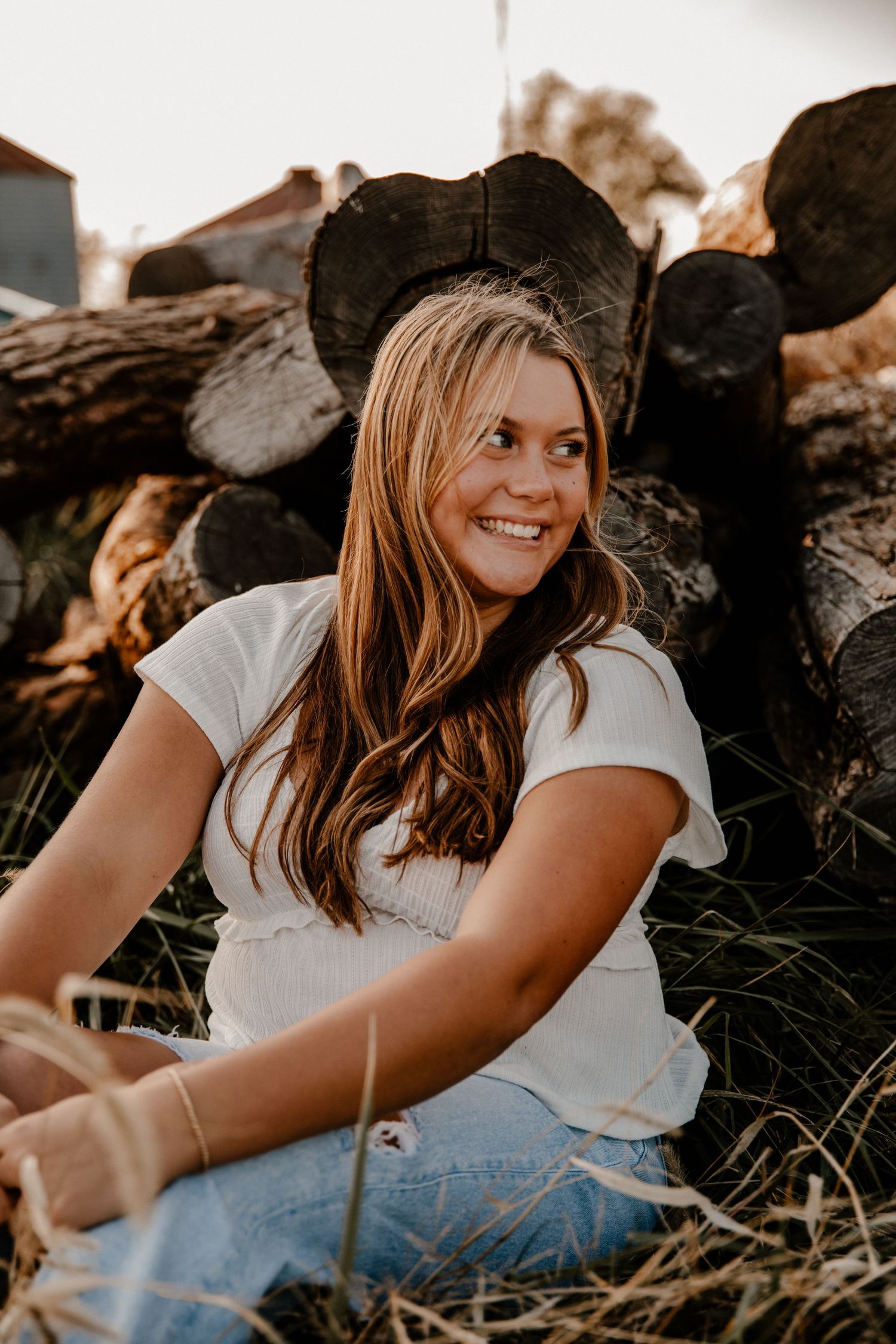 Casual outdoor portrait session with rustic wooden logs and natural lighting.