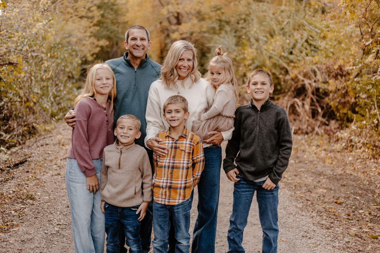 Group portrait of family members smiling together on autumn trail.