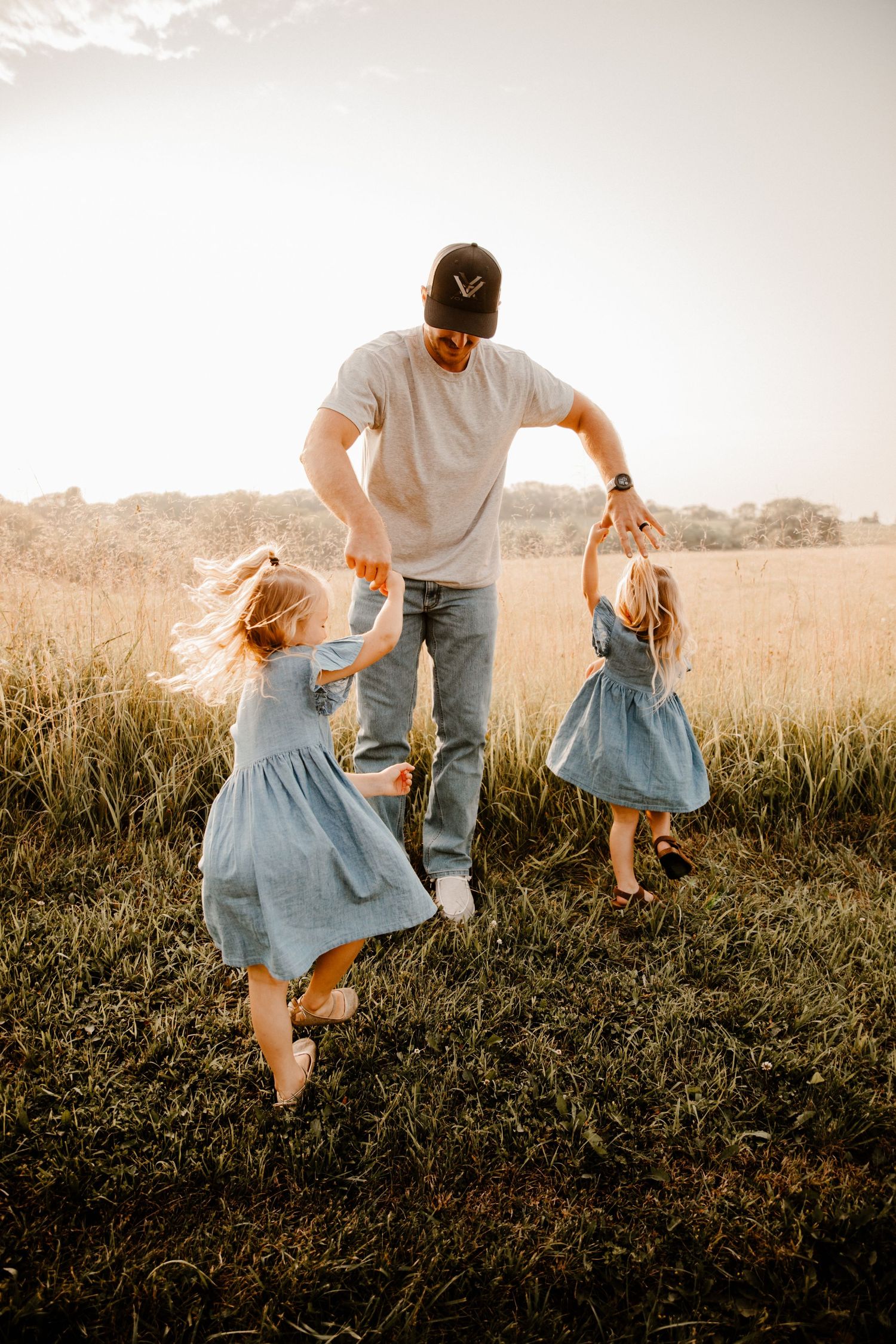 Playful family moment captured in a field during golden hour wearing matching denim and white.