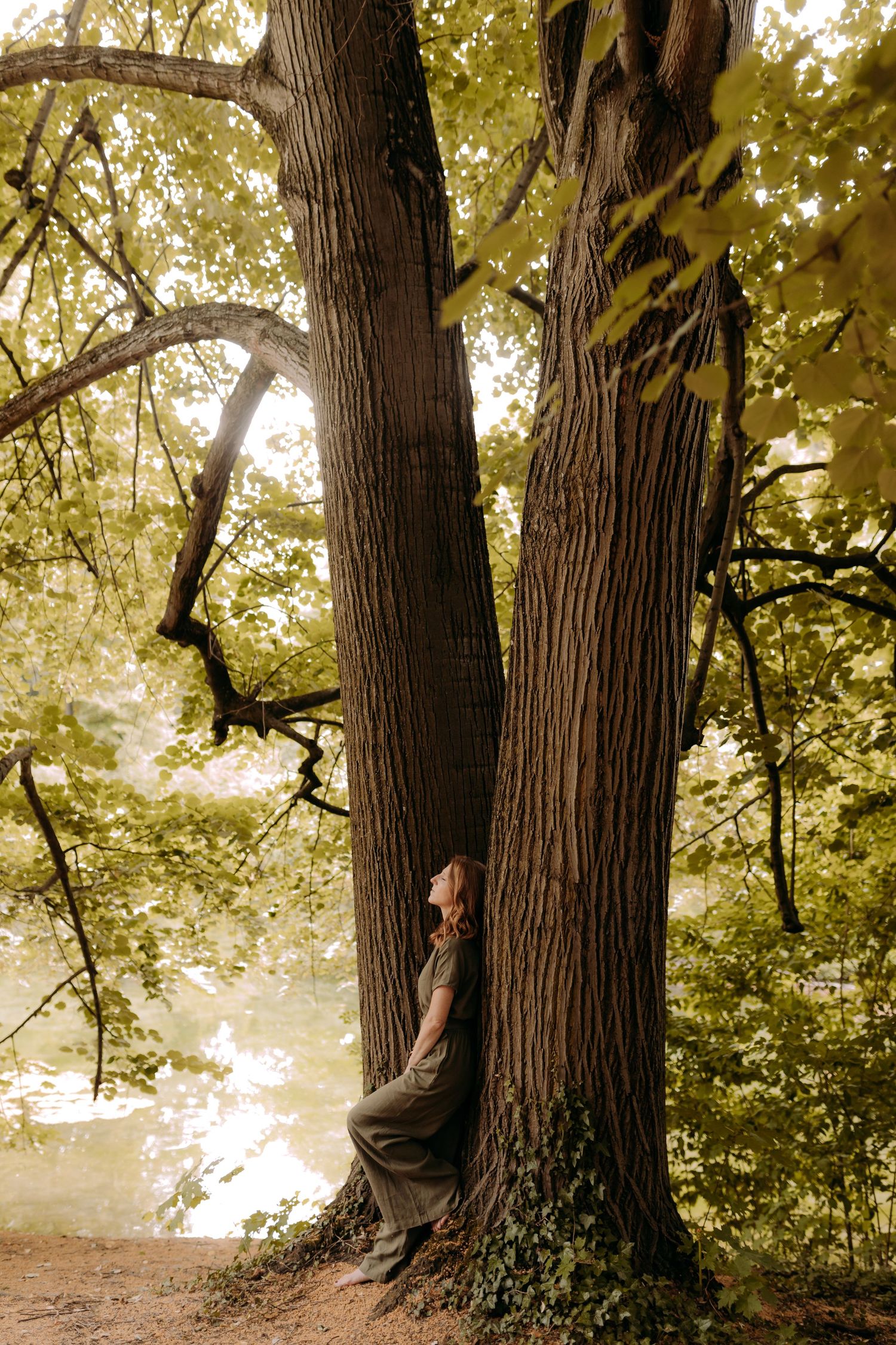 Praticienne en Reïki adossée à un grand arbre en pleine nature pour une séance d'ancrage énergétique et de reconnexion à soi.