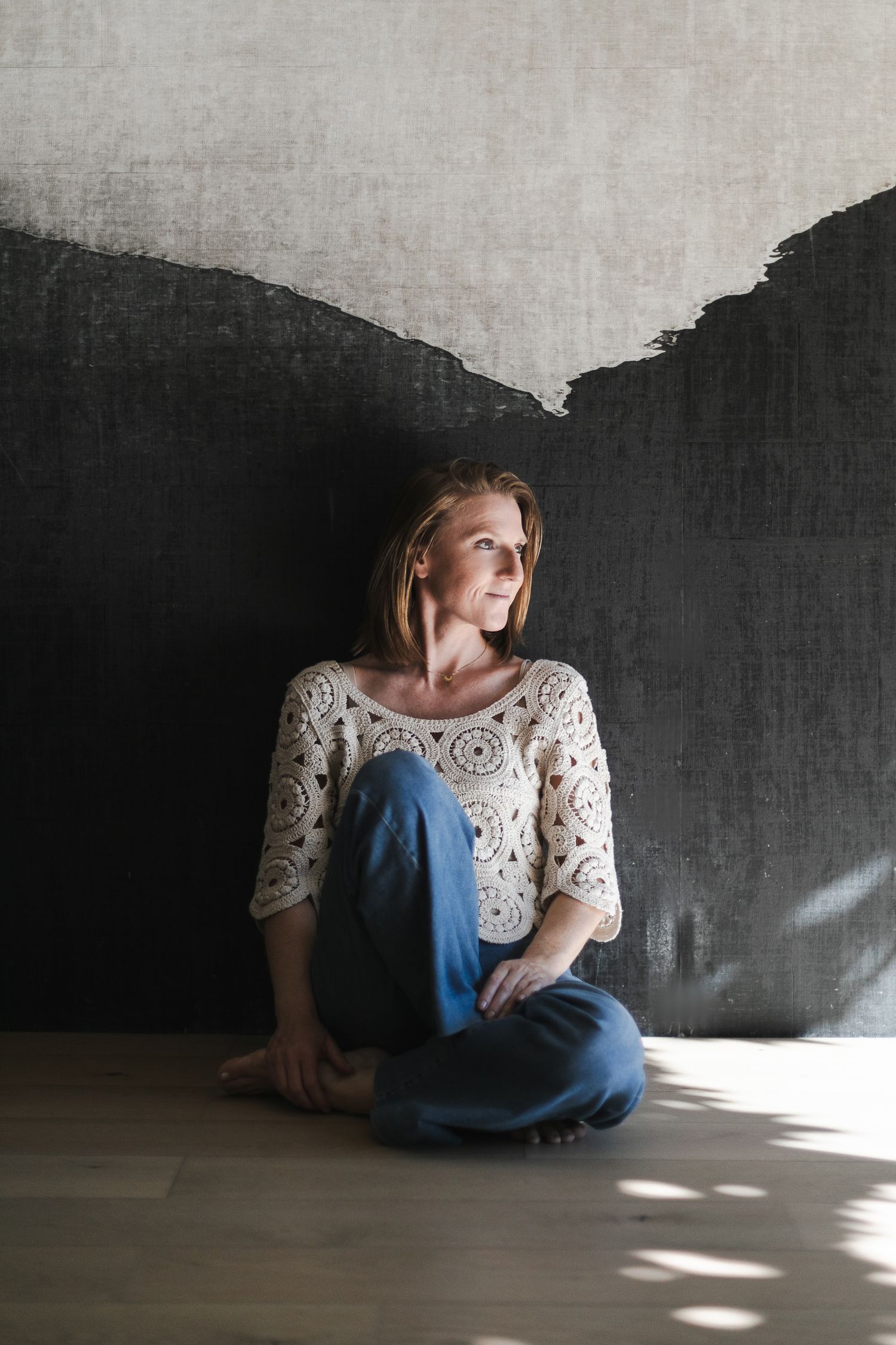 Praticienne massage bien-être assise contre un mur, le regard au loin. Elle dégage calme, sérénité, douceur, amour et bienveillance.