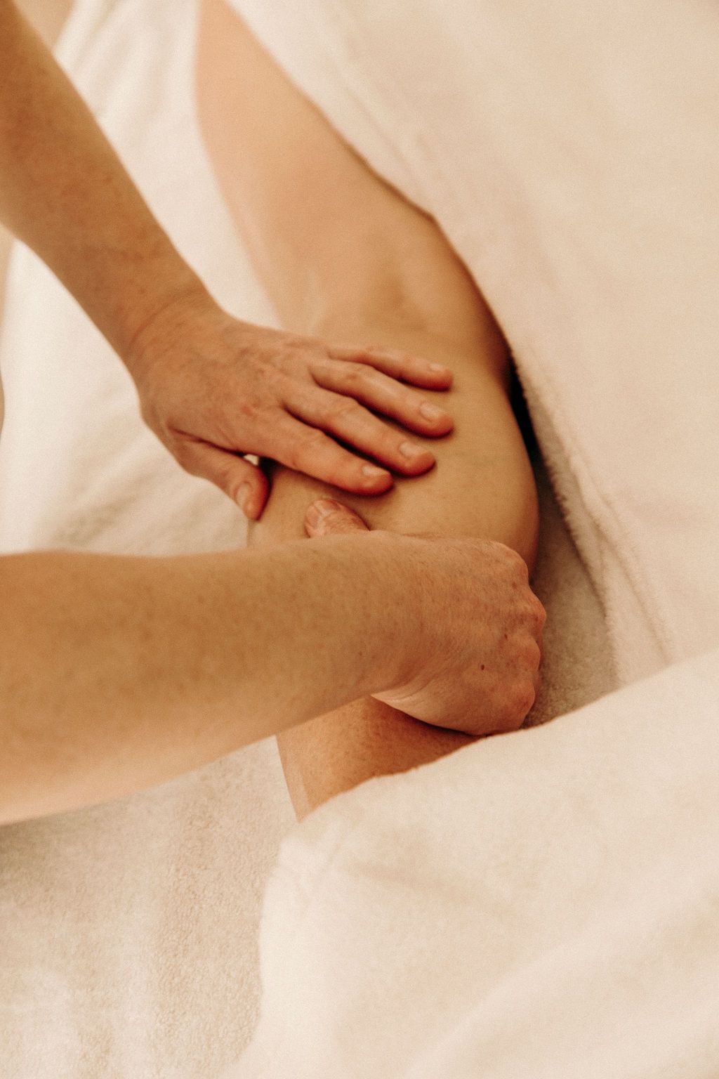 Deux mains posées sur un mollet avec huile de massage pour dénouer et détendre la zone. Massage postnatal doux et relaxant.
