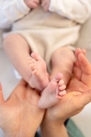 Deux petits pieds nus d'un bébé positionnés au creux des mains de sa maman. Douceur et bien-être bébé ouest lyonnais.