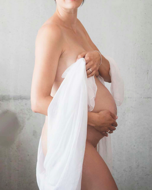 Corps de femme enceinte avec drapé blanc qui tombe le long de son corps. Main posée sur le ventre avec douceur.