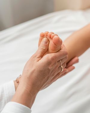 Main d'une maman entrain de masser la voûte plantaire du pied de son enfant. Massage pied avec douceur, bienveillance et amour pour apaiser