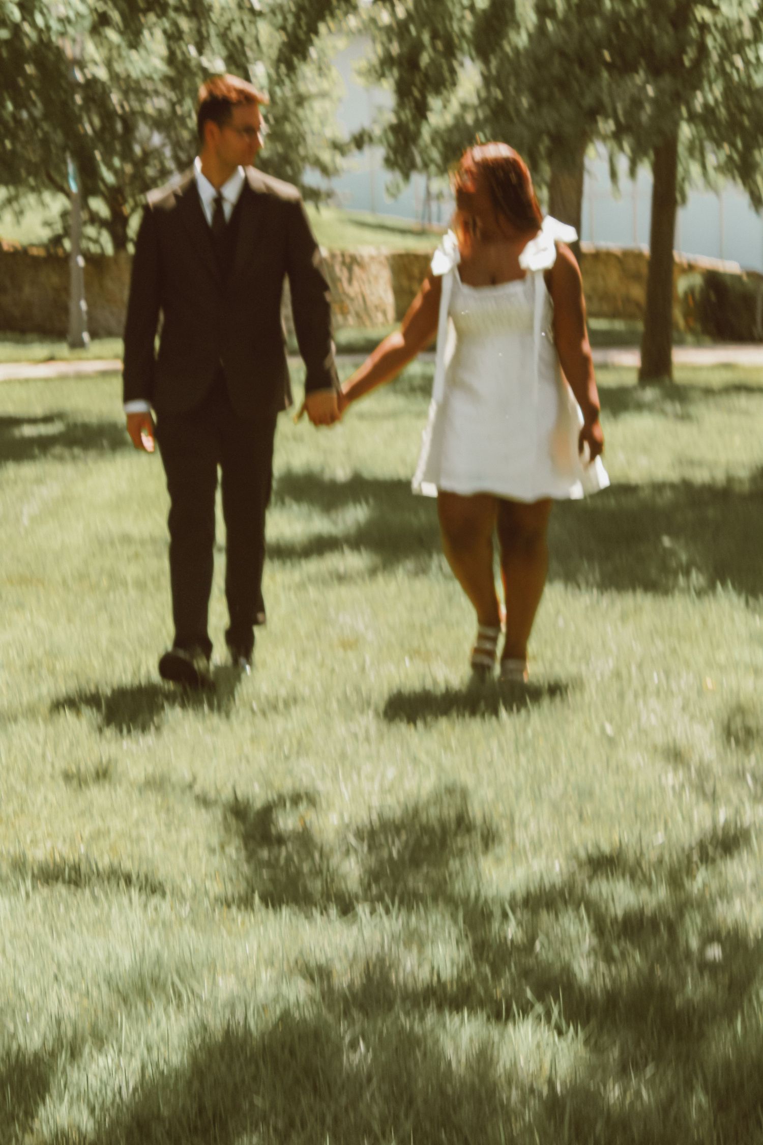 A couple walks together on a sunny day through a grassy park in vintage-style photography.