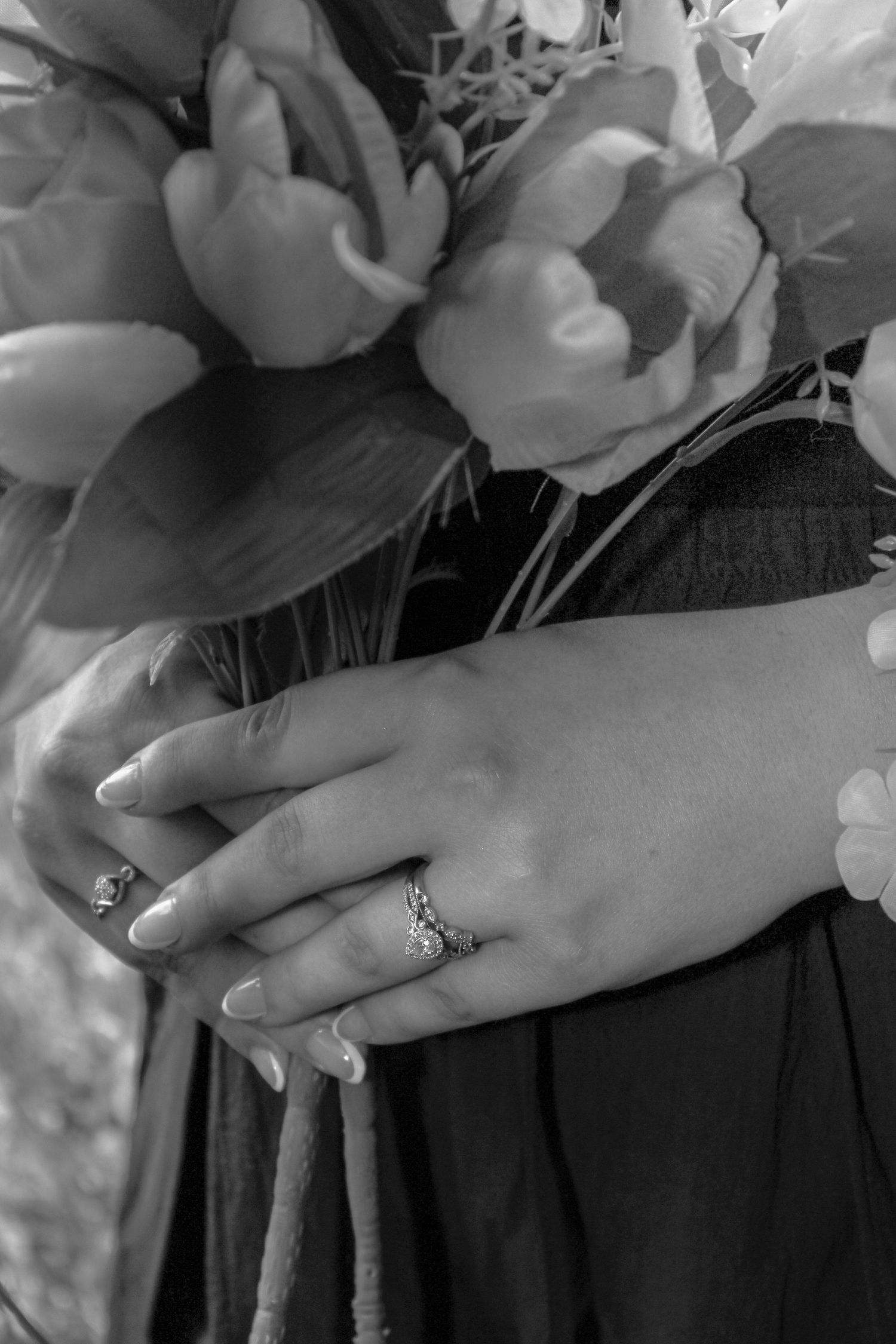 Close-up black and white photo of hands with an engagement ring surrounded by roses.