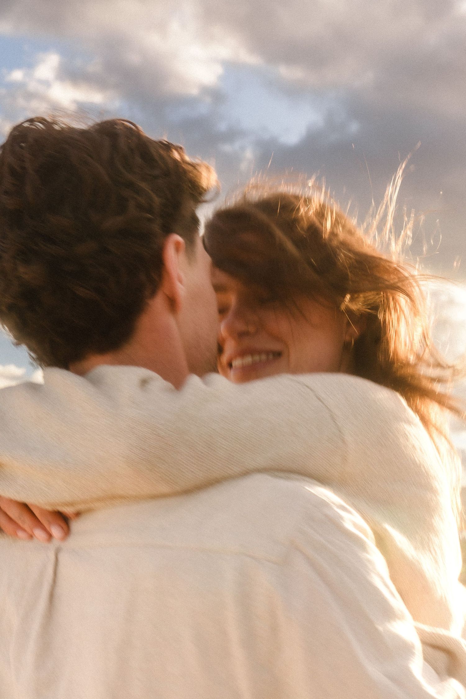 Couple in white embracing against a dramatic sunset sky.