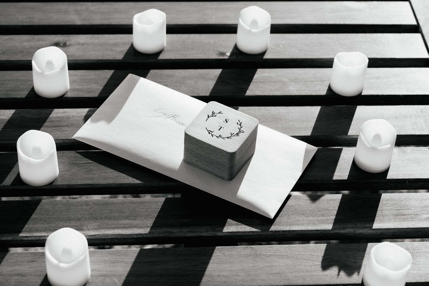 White candles arranged around a small box on a striped wooden surface.