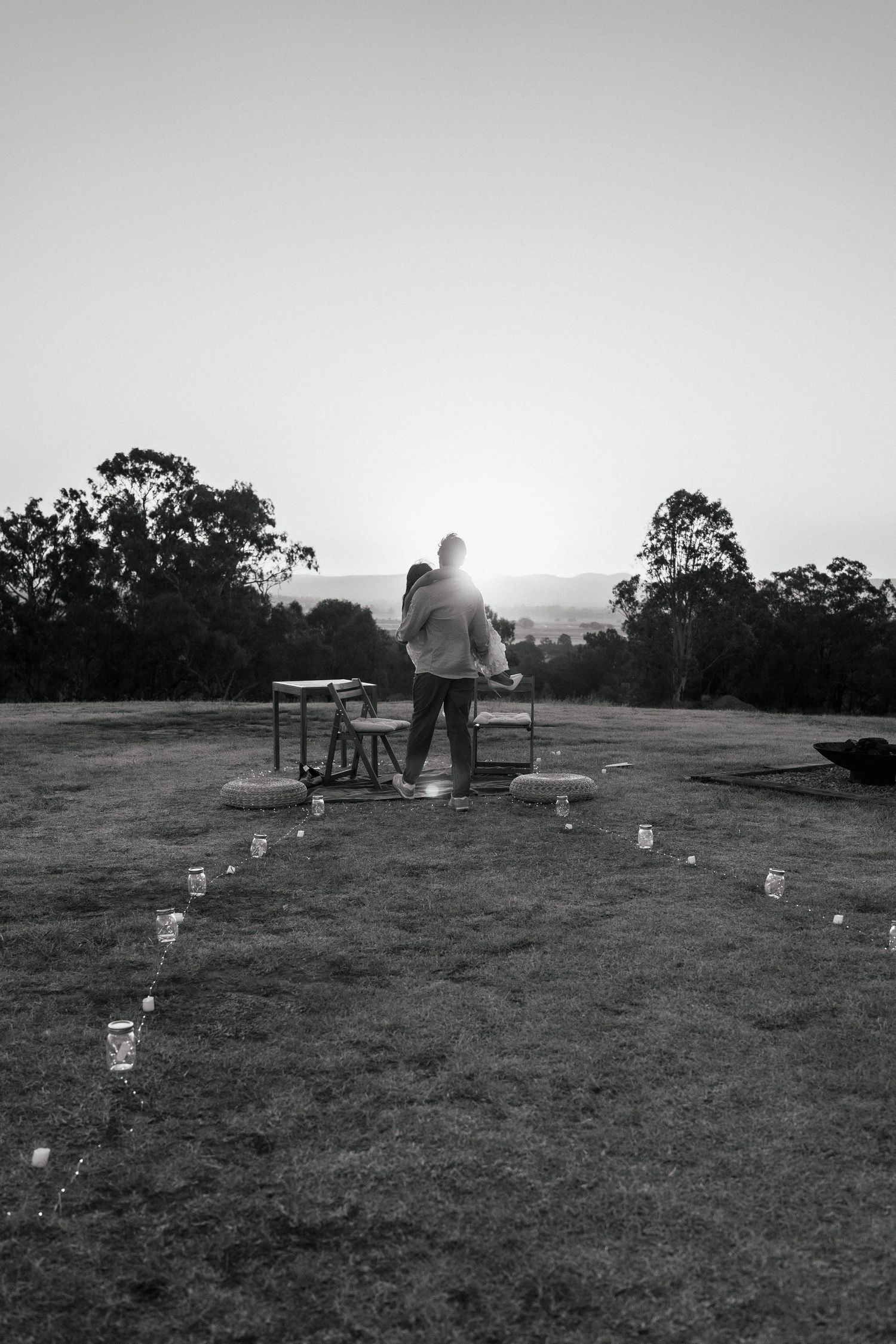 Romantic hilltop scene with glowing lanterns arranged around a wooden picnic table at dusk.