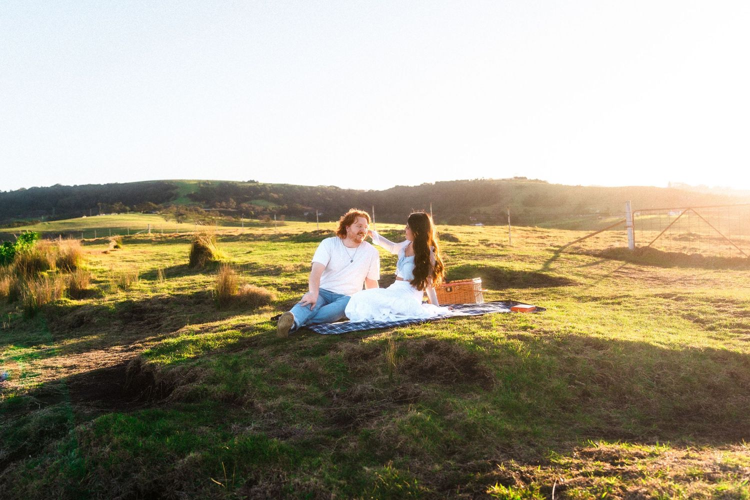 Panoramic sunset view of a couple having a picnic on a hilltop meadow.