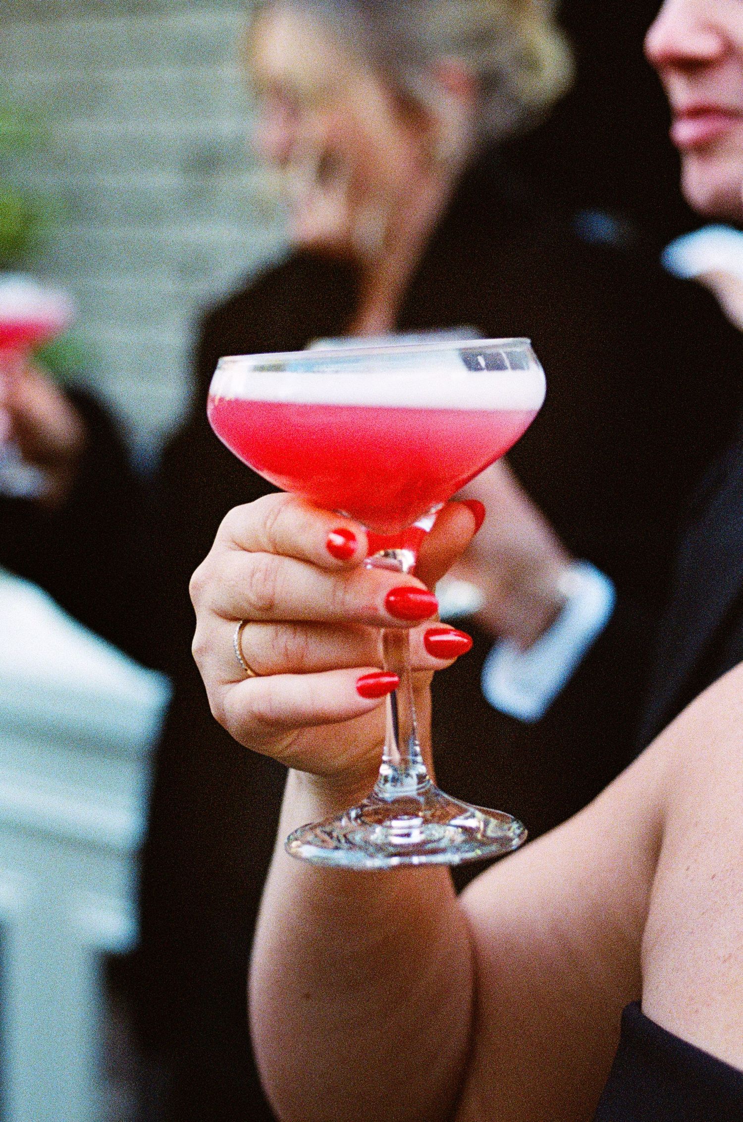 Close-up of hands holding pink cocktails in coupe glasses at a wedding reception.
