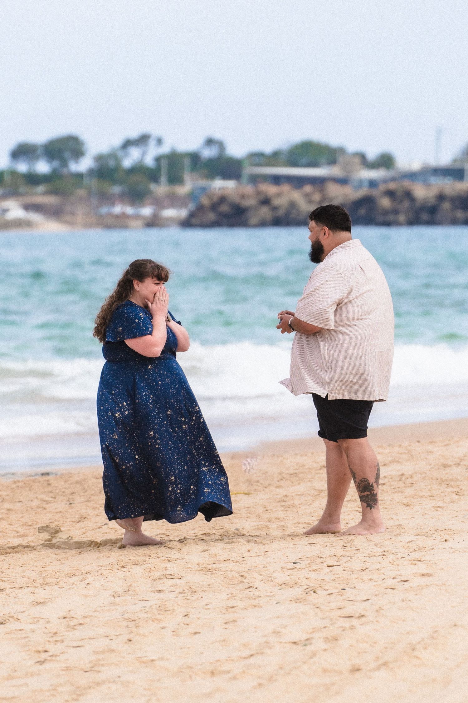 Two people sitting close together on a sandy beach with ocean waves in the background.