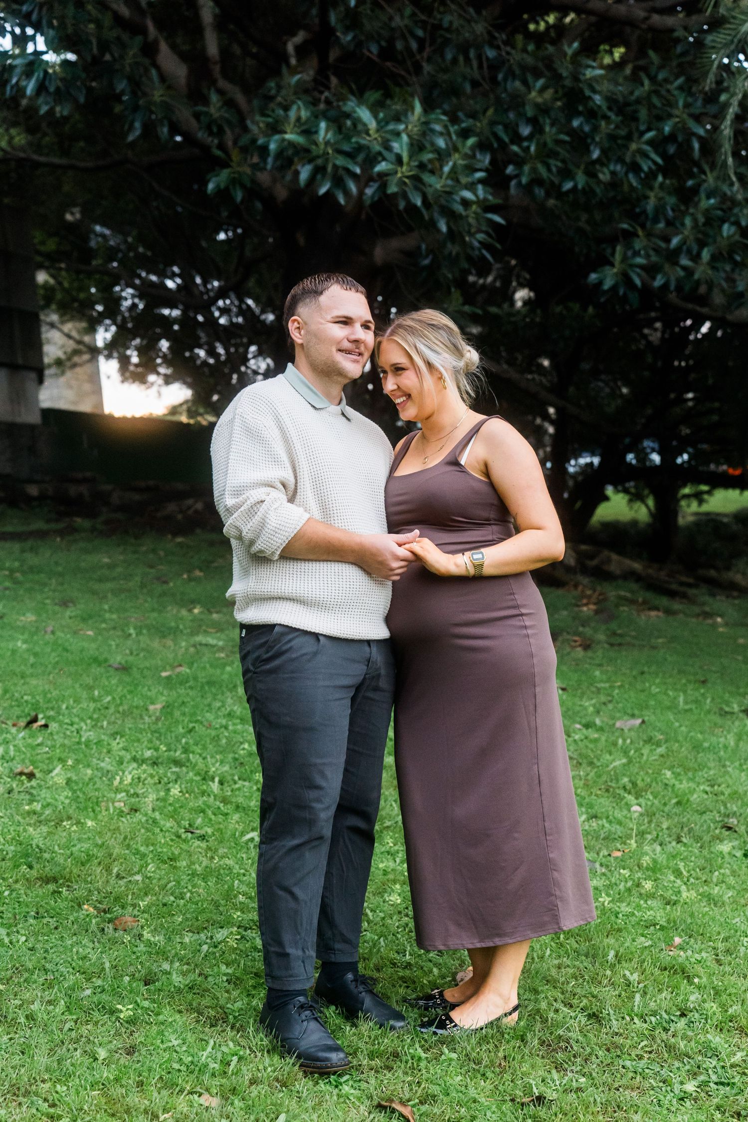 A couple poses together on a grassy lawn during an engagement photoshoot.